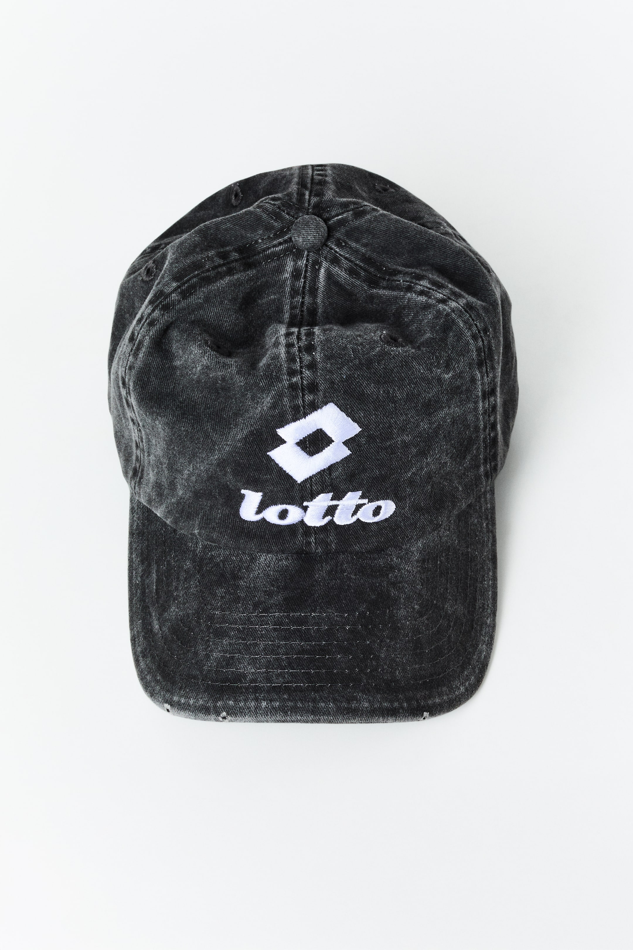 Ampliar la imagen: Una gorra de béisbol en negro lavado presenta un logo Lotto bordado en blanco y texto en su parte frontal, mostrando una visera curva y un botón superior.