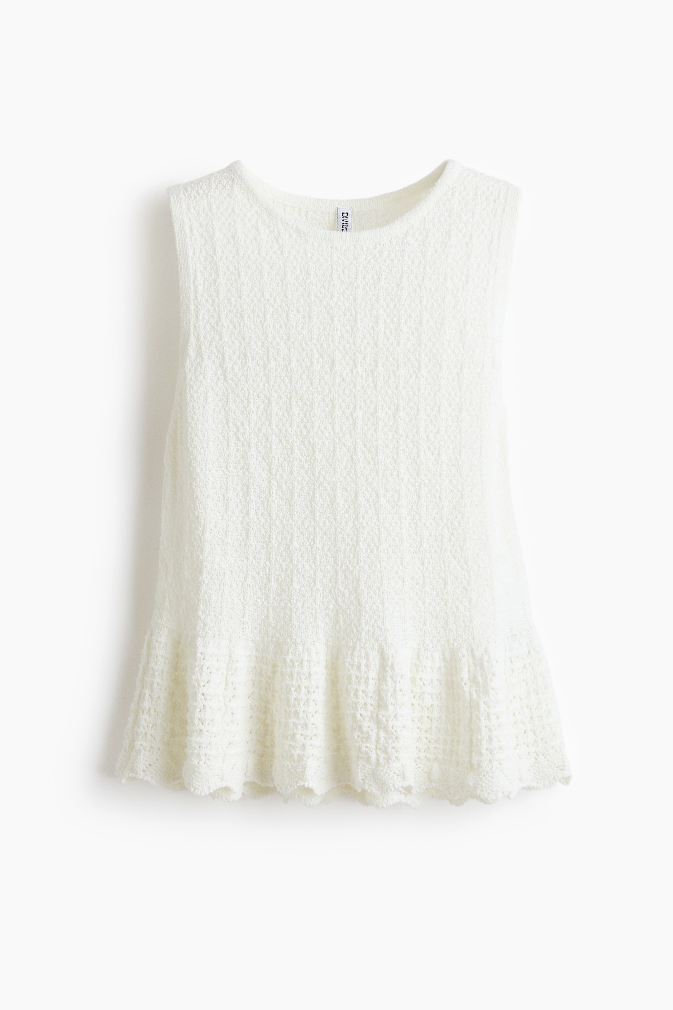 View larger image: A white sleeveless knit top featuring a round neckline and a textured main body with subtle vertical patterning. The top flares at the bottom, culminating in an open-knit, scalloped hem.