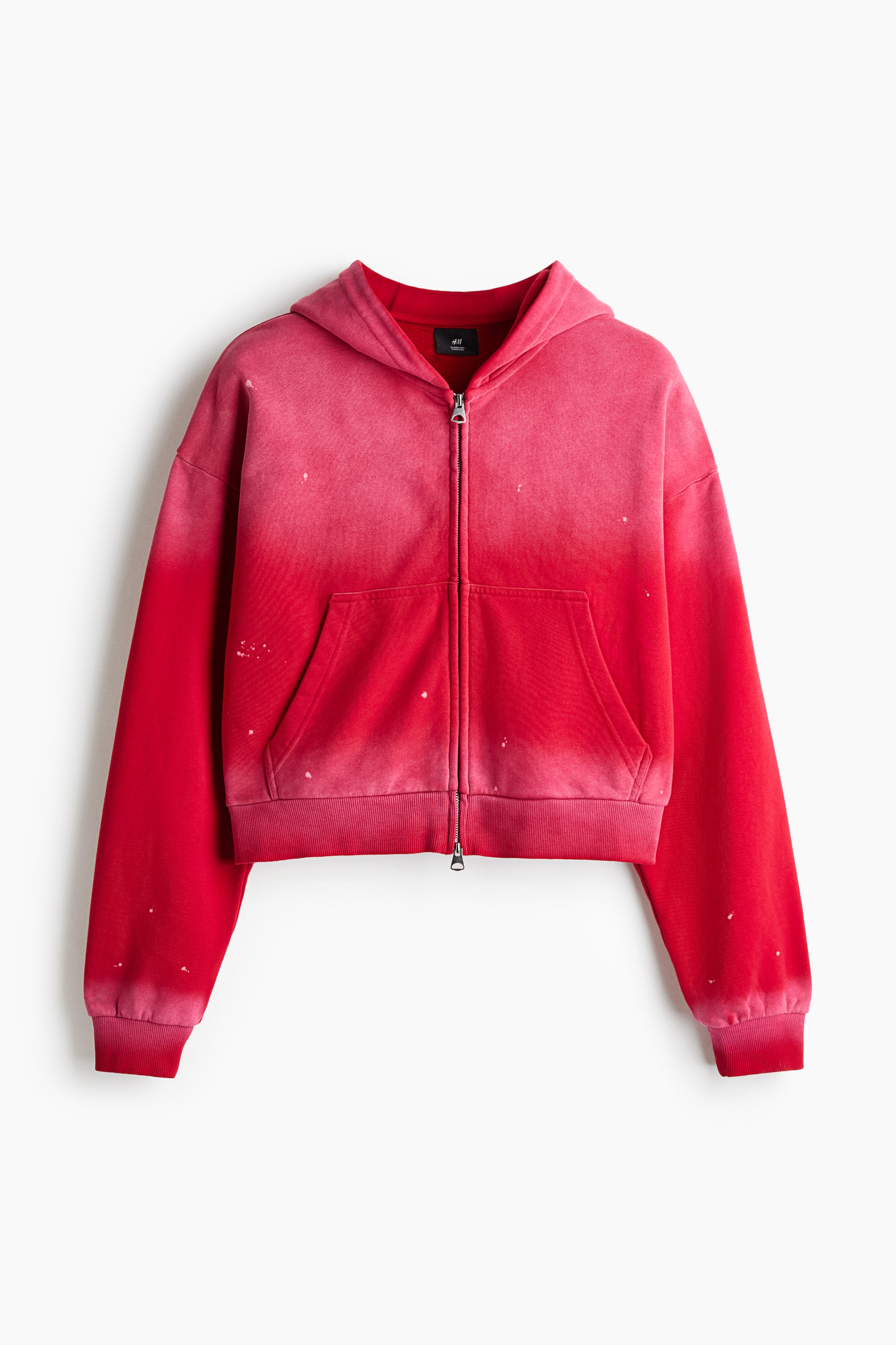 Xem ảnh lớn hơn: Một chiếc áo hoodie kéo khóa dáng boxy với hiệu ứng loang màu chuyển từ đỏ sang hồng đang được chụp chính diện, thể hiện phom dáng oversized với vai trễ và tay áo dài. Áo hoodie được thiết kế khóa kéo hai chiều ở mặt trước, túi trước chia đôi và chi tiết bo rib ở cổ tay cùng gấu áo.