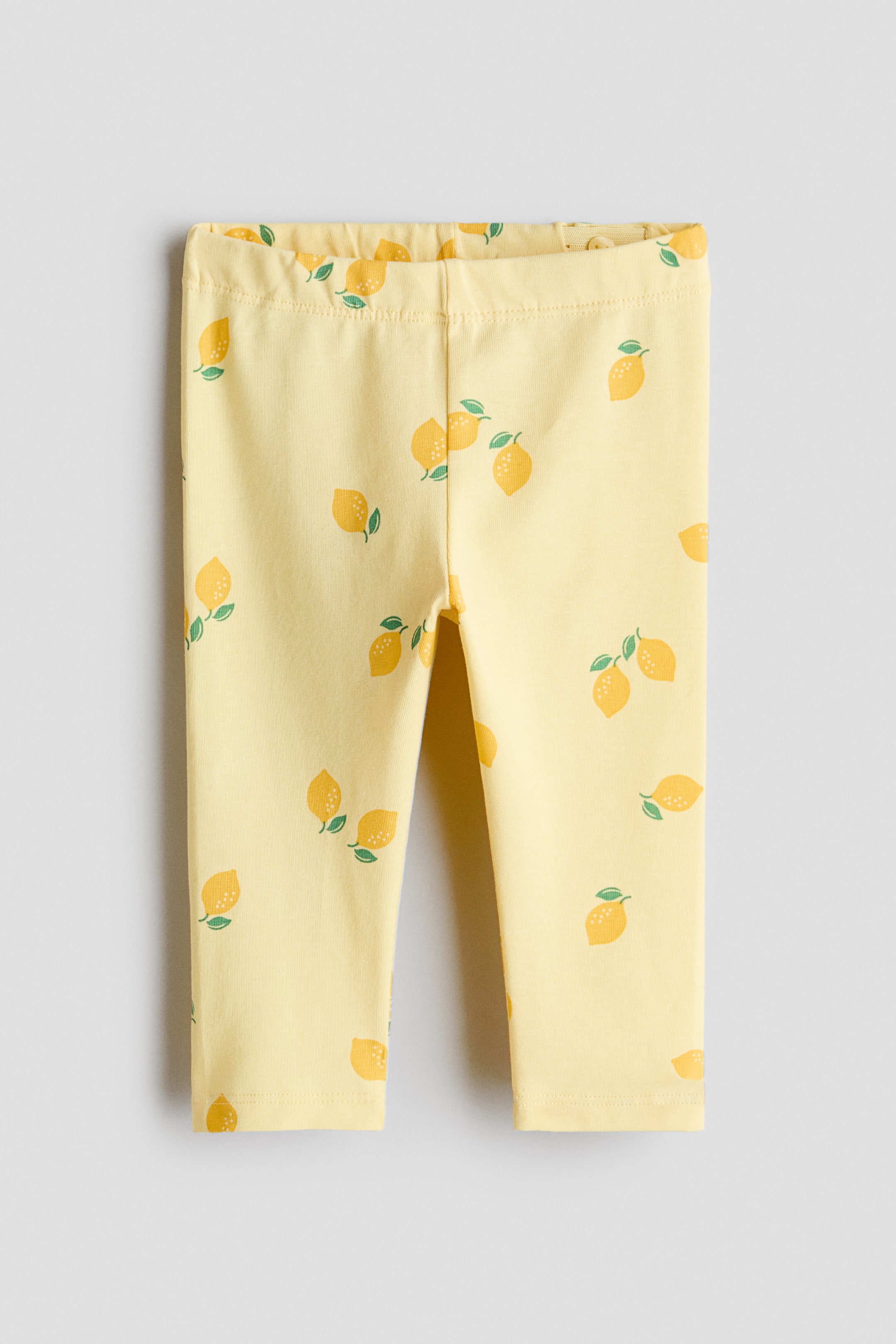 Ver imagem maior: As leggings amarelas exibem uma estampa integral de limões dispersos com folhas verdes, apresentadas de frente. Apresentam um cós elástico franzido e pernas afuniladas.