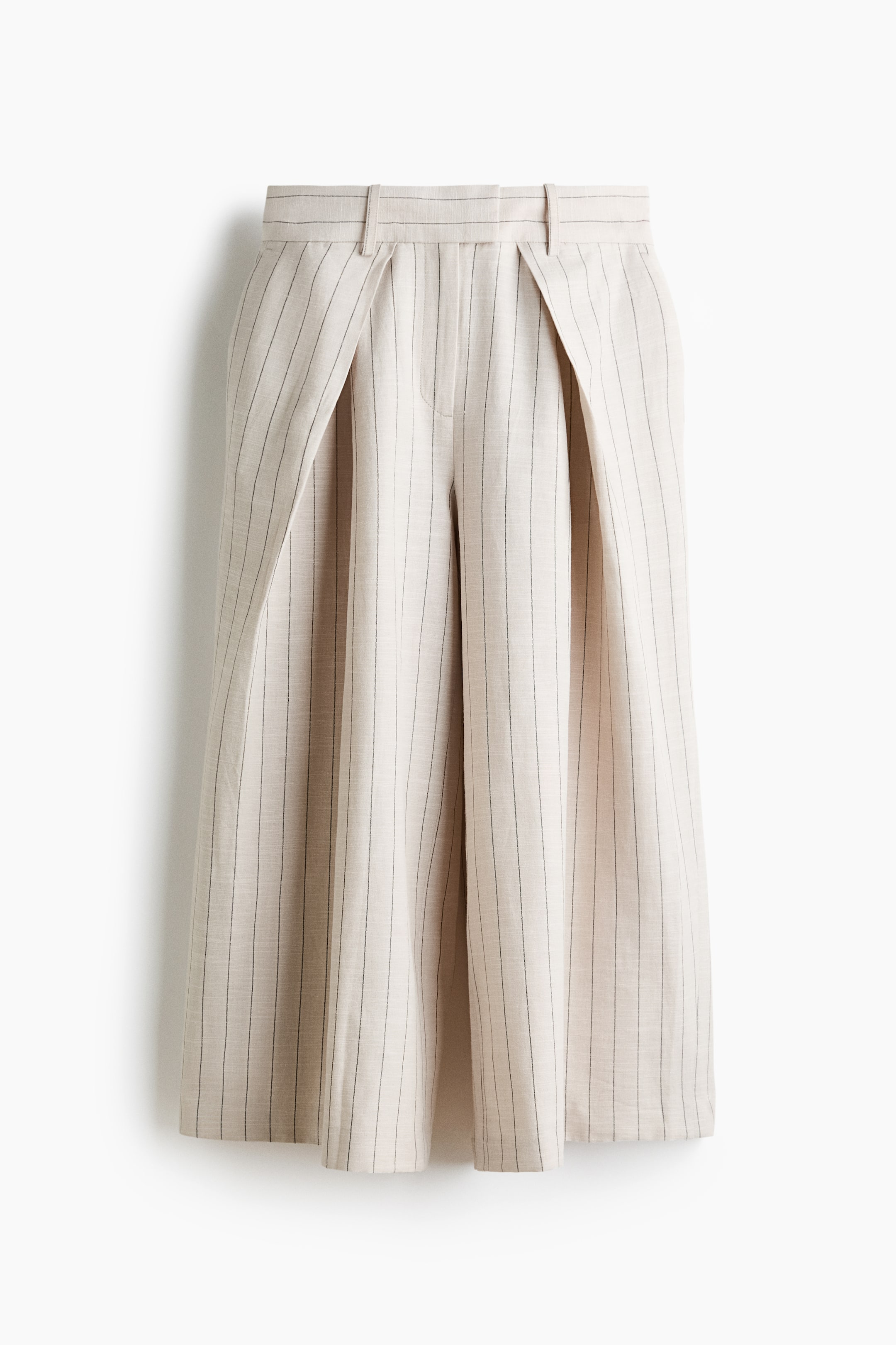 Grotere afbeelding bekijken: Culottes in lichtbeige geweven stof met dunne donkere verticale strepen worden van voren gepresenteerd. Ze hebben een platte tailleband met riemlussen, een voorsluiting met rits, opvallende plooien vooraan en wijde pijpen met overslagzijden.