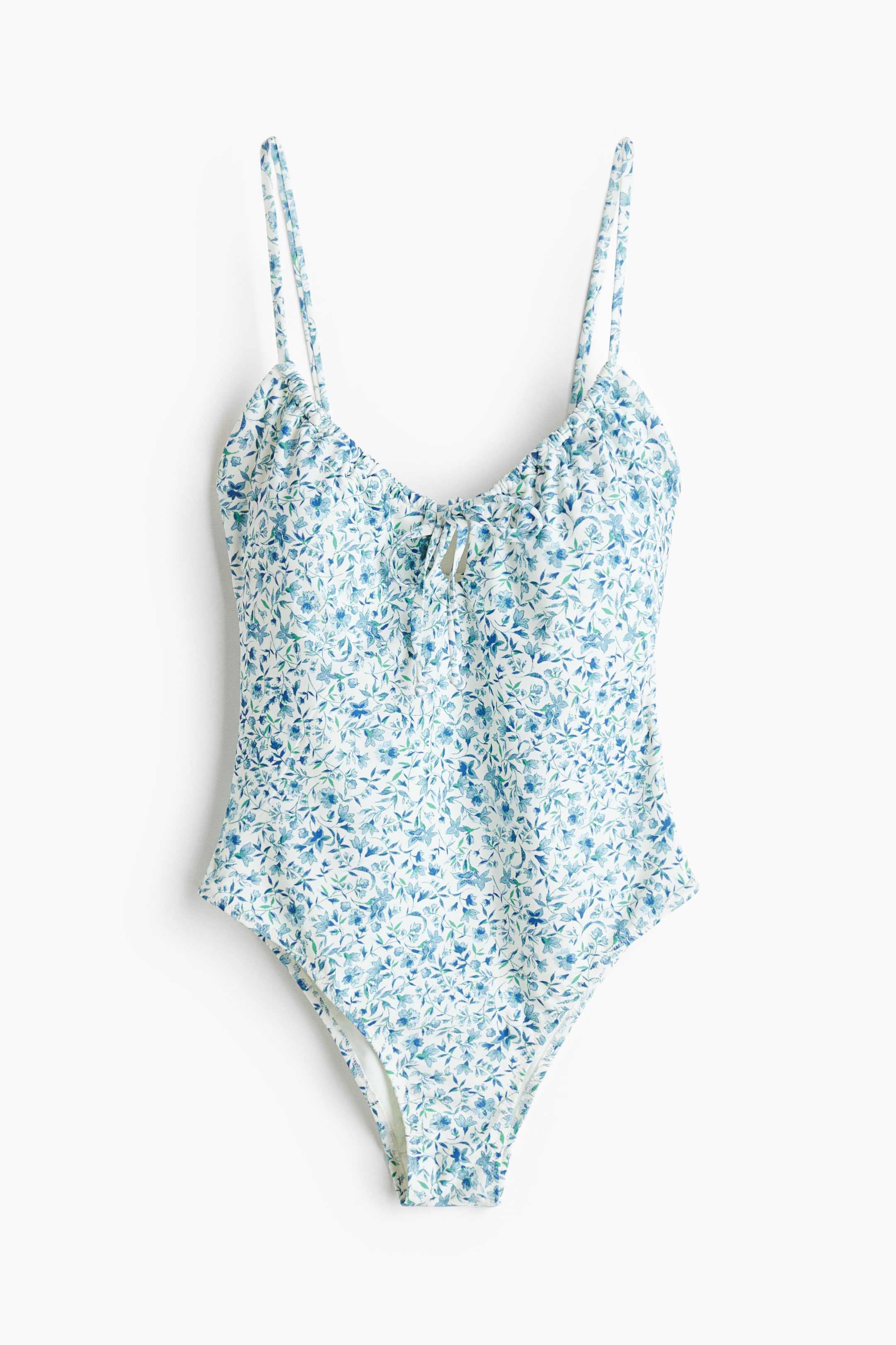 View larger image: A one-piece swimsuit showcases a blue and green floral pattern on a white background, facing front. It features thin spaghetti straps, a ruched bust with a central tie detail, and a high-cut leg.