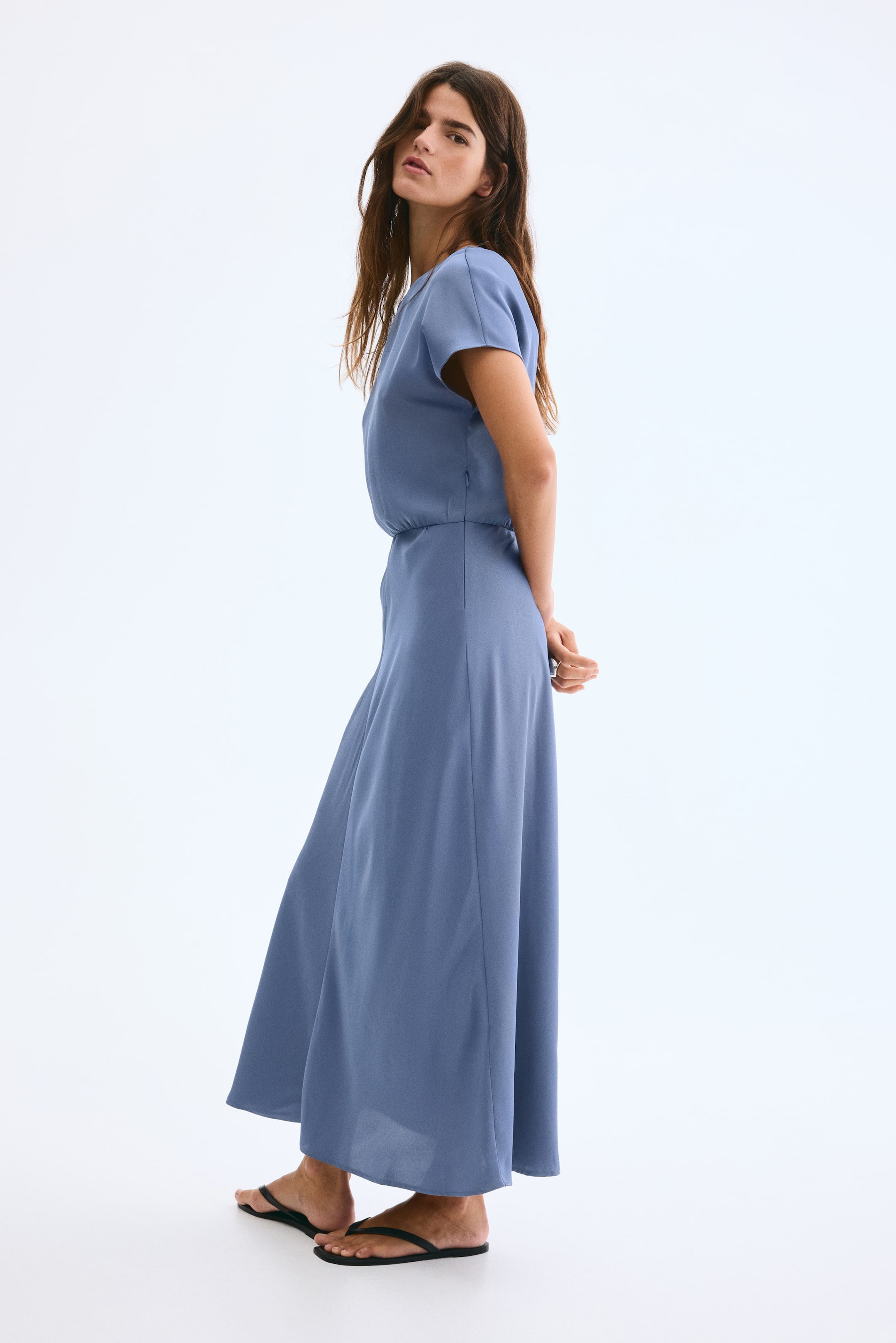 View larger image: A slate blue maxi dress is presented from a side-back angle, featuring short sleeves, a round neckline, and a gathered waist flowing into an ankle-length skirt.