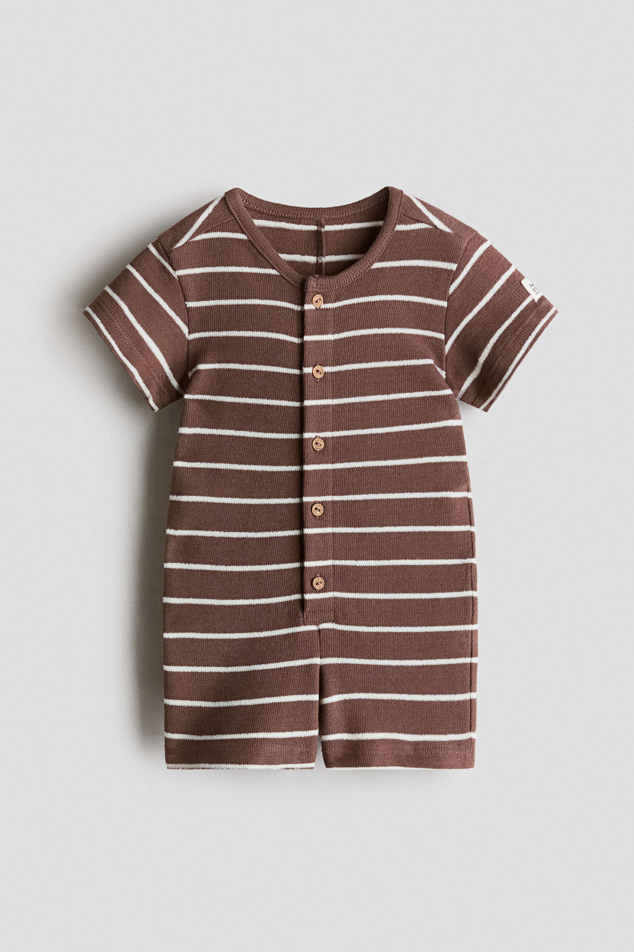 View larger image: The baby romper is displayed front-facing, showcasing brown and white horizontal stripes, with short sleeves, a round neckline, and short legs. A full-length button placket adorned with circular wooden buttons runs down the center front.