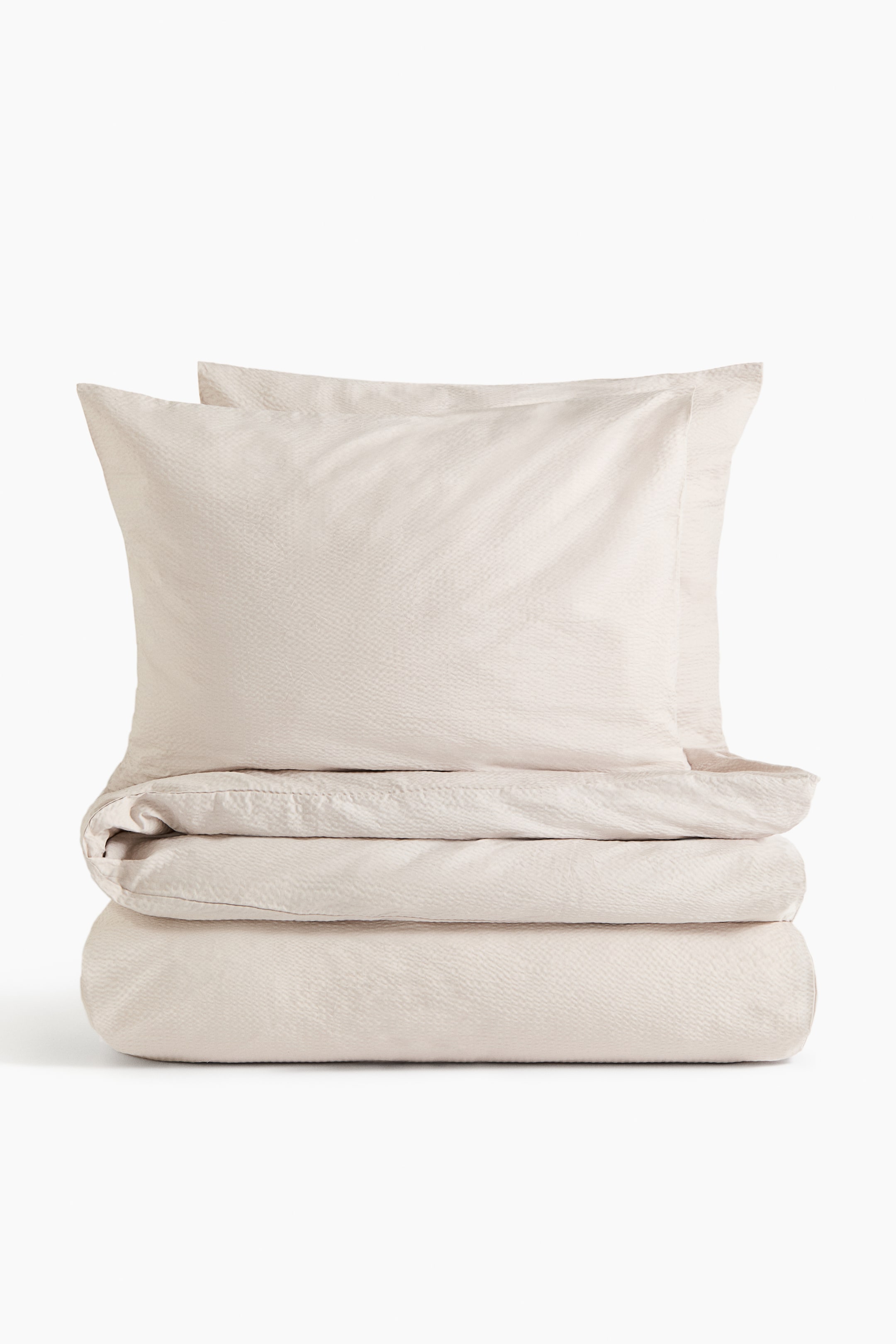 View larger image: The double duvet cover set showcases a light beige hue with a unique seersucker texture. The duvet cover is folded horizontally, with two pillowcases stacked vertically behind it, all facing forward.
