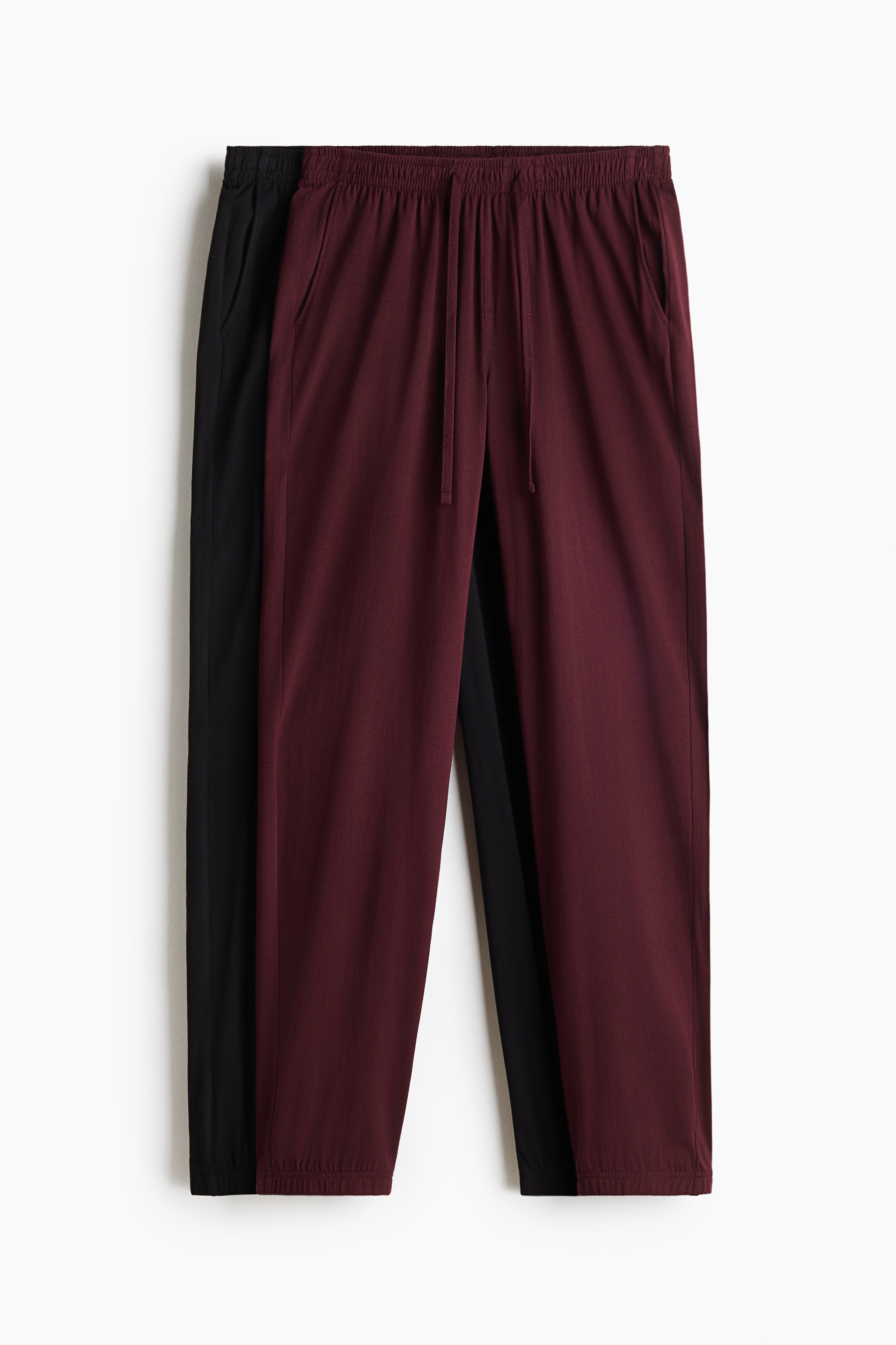 Black cotton jersey track pants featuring a regular fit, an elasticated drawstring waist and ribbed hems are being worn by the model. The trousers are paired with a matching black long-sleeved top featuring white trim at the collar and hem.