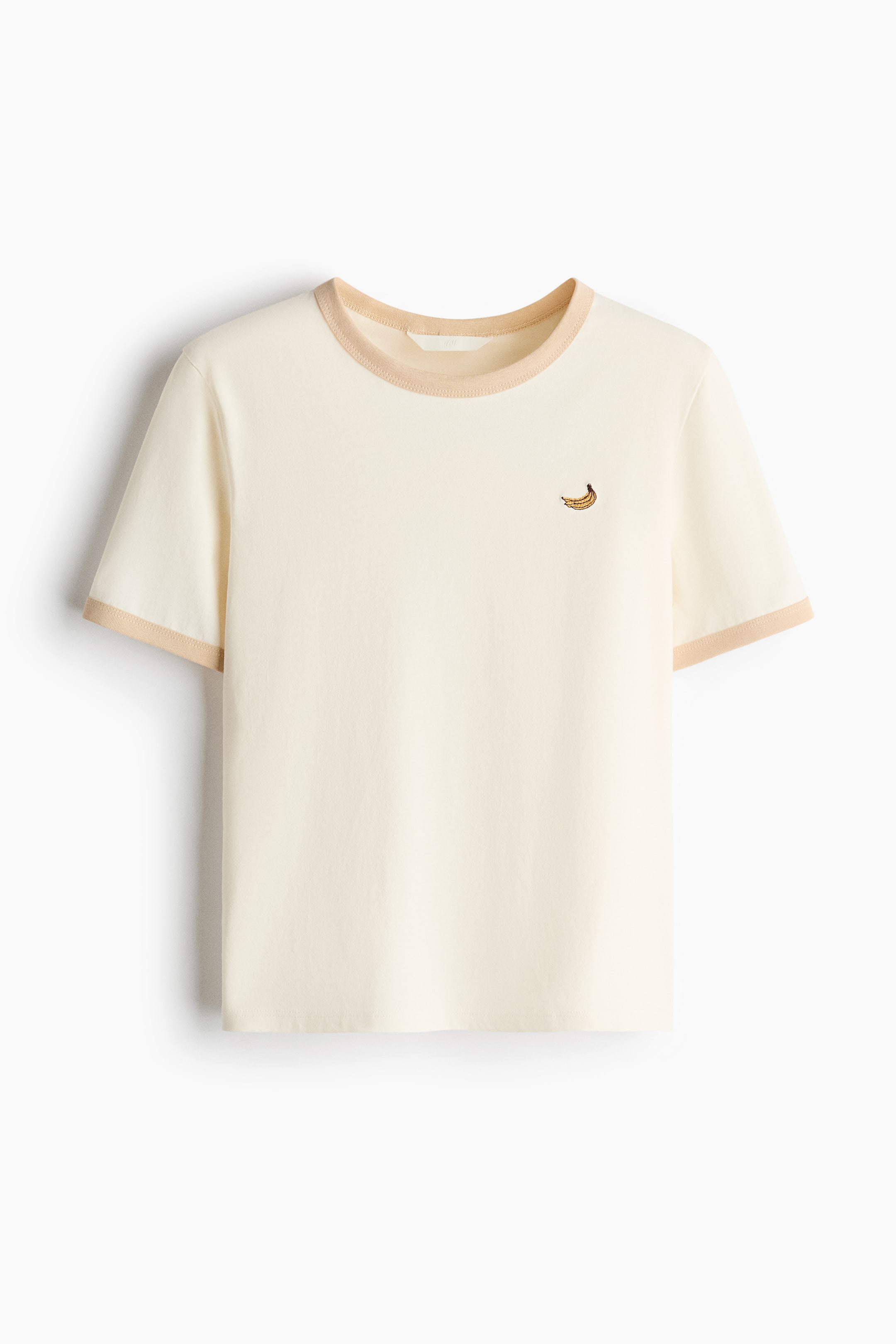 View larger image: A cream short-sleeved t-shirt featuring a round neck and short sleeves, both with beige ribbed trims. A small embroidered banana motif adorns the left chest.