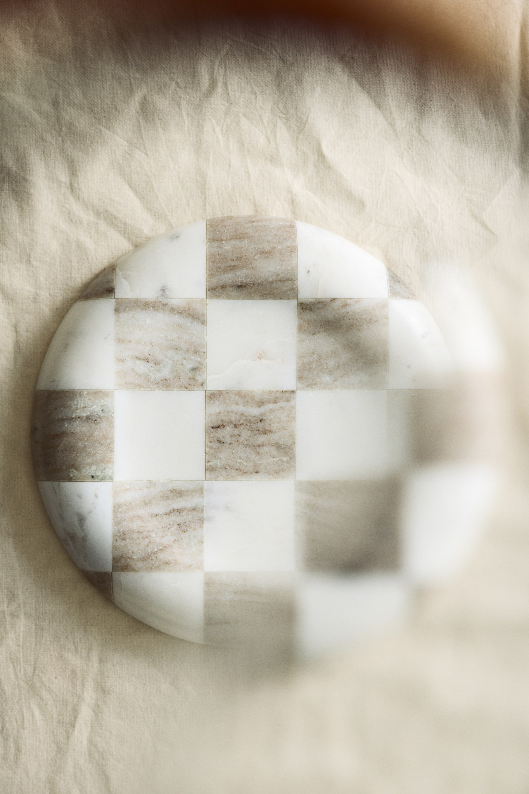 View larger image: A round marble board displays a chequered pattern. It is composed of alternating squares of white marble and brown-grey veined marble, laid flat and viewed from above.