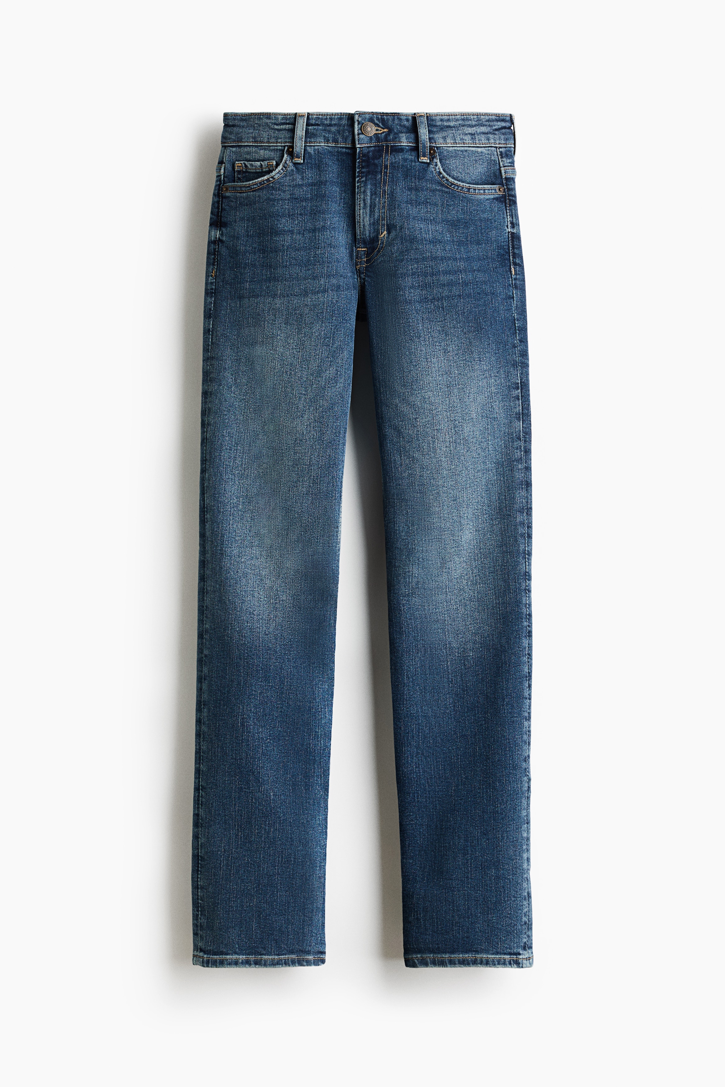 These dark blue five-pocket jeans are being worn by the model, showcasing a regular fit from the waist to the thighs and a slim fit from the knees to the hems. The jeans are styled with a black leather jacket and black heeled sandals, ending at the feet with minimal stacking.