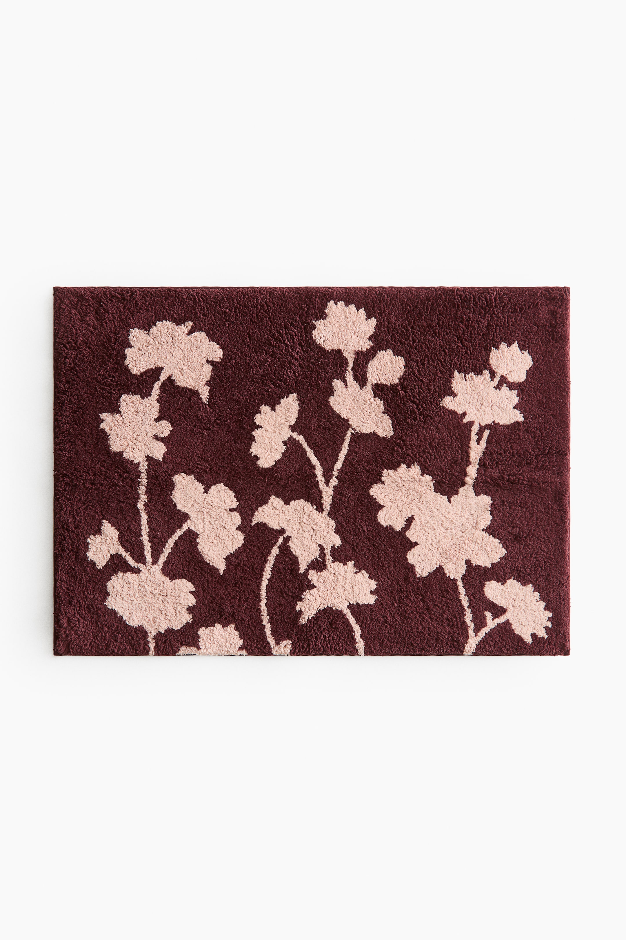 View larger image: A rectangular bath mat is lying flat, displaying a light pink floral pattern on a dark reddish-brown tufted cotton weave.
