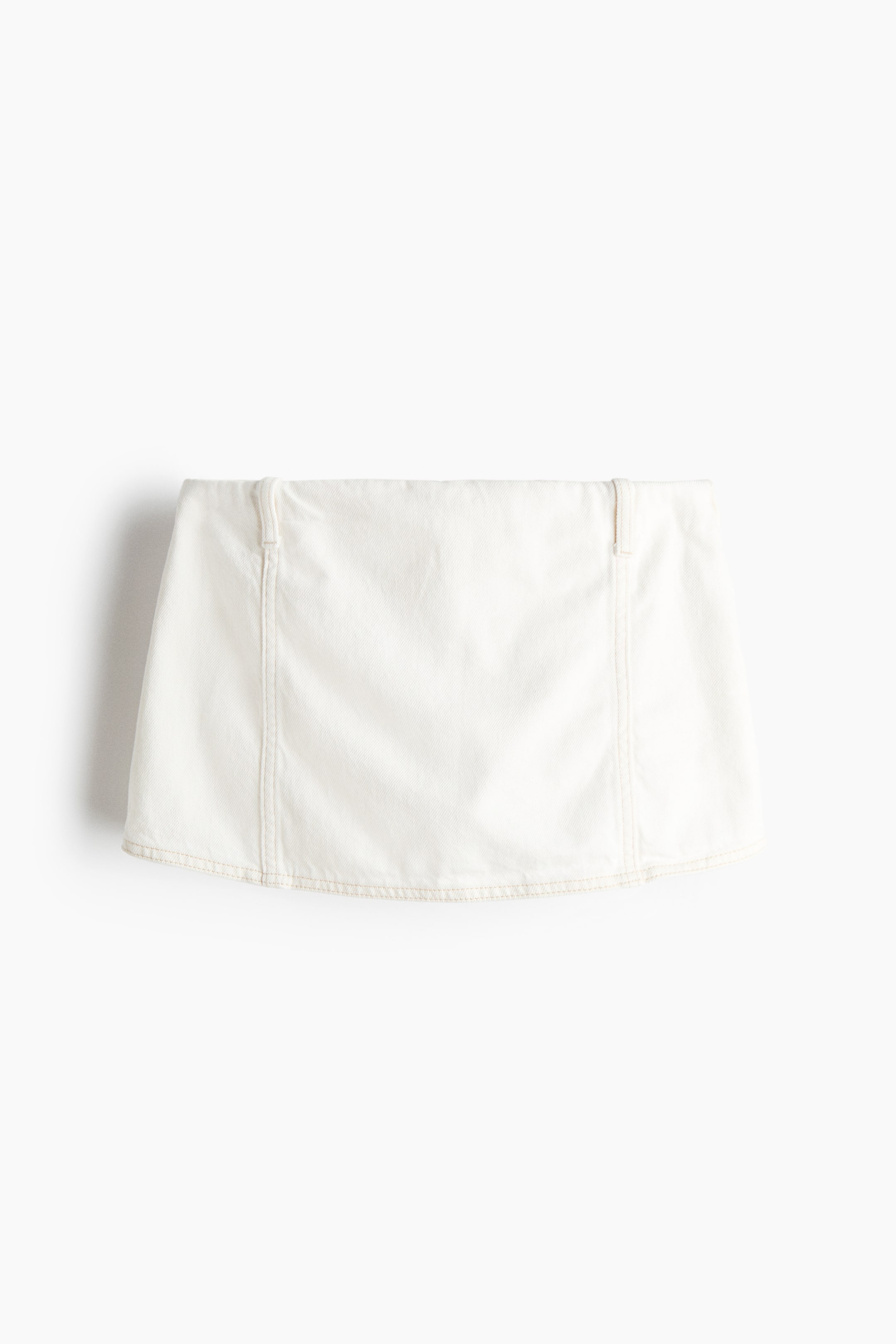 View larger image: A white mini skirt is shown from the front, featuring visible tan stitching along the vertical seams and hem. It also has a flat waistband with belt loops at the sides.