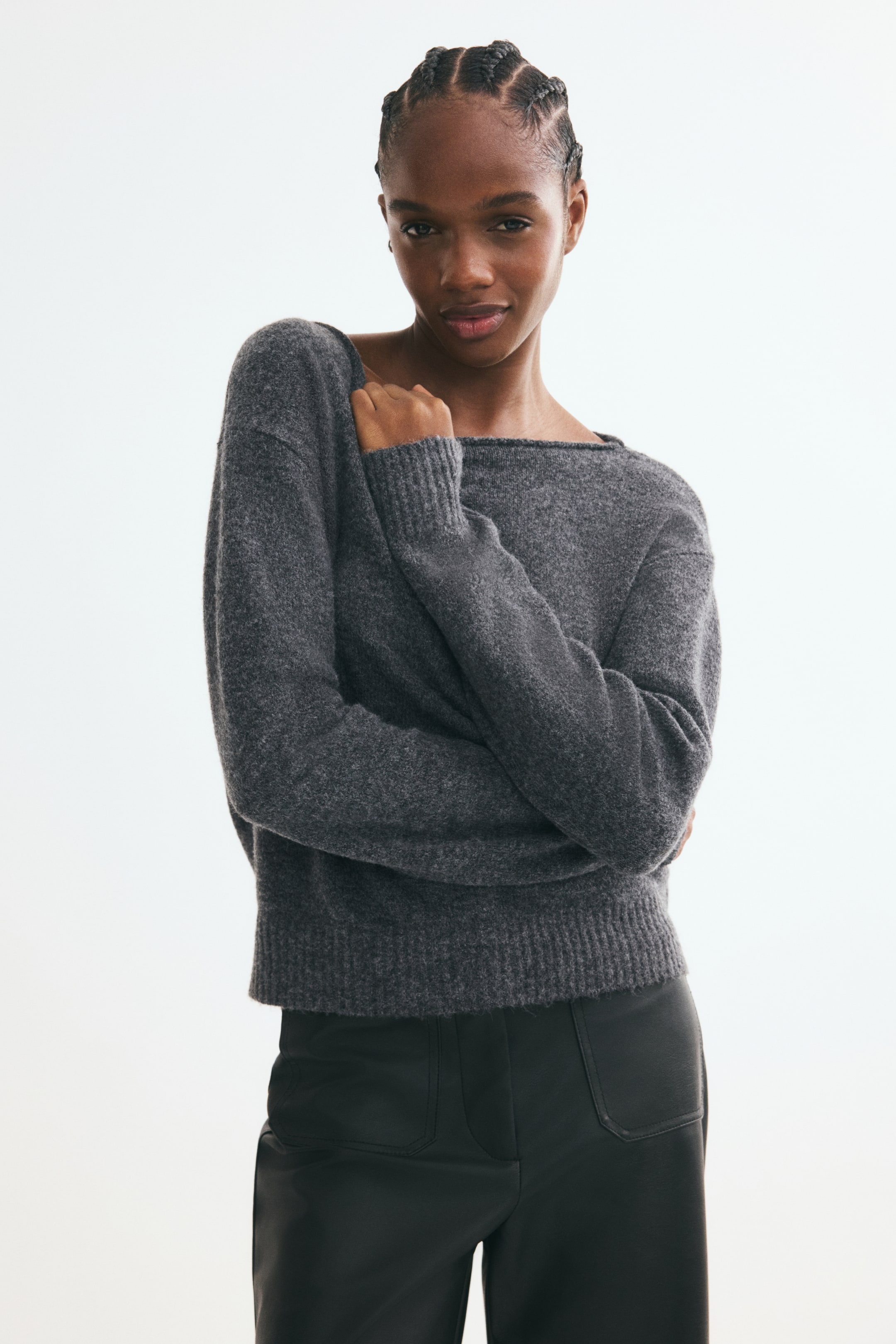 View larger image: The model is wearing a grey knit sweater with a brushed finish, boat neck, dropped shoulders, and ribbed trim, styled with black pants. The model is posed with arms crossed over the chest.