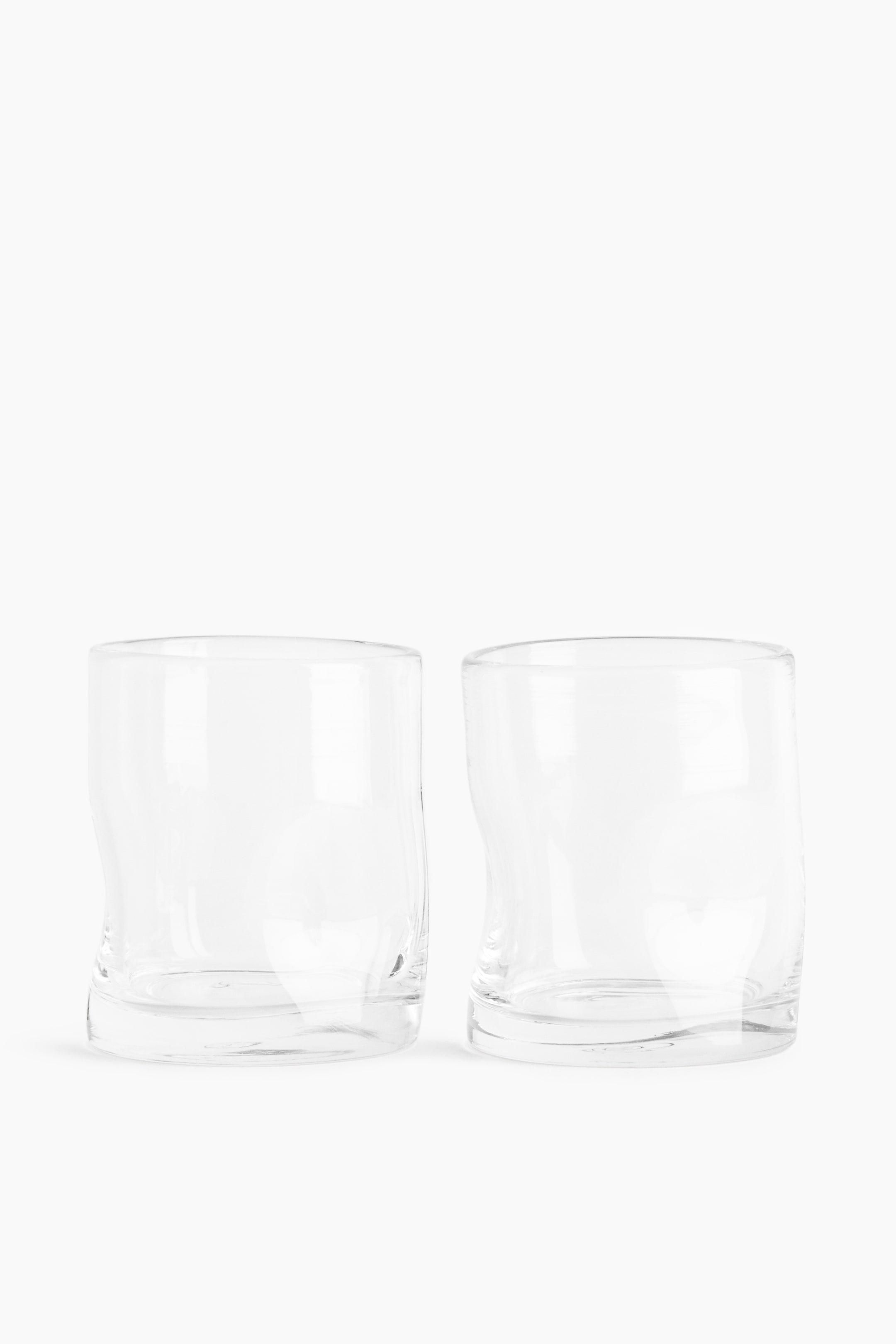 拡大画像を表示: 2つの透明なガラス製タンブラーが前面を向いており、それぞれが微妙に不規則なデザインと柔らかく丸みを帯びた縁を特徴としています。厚手のガラスで作られており、容量は300mlです。
