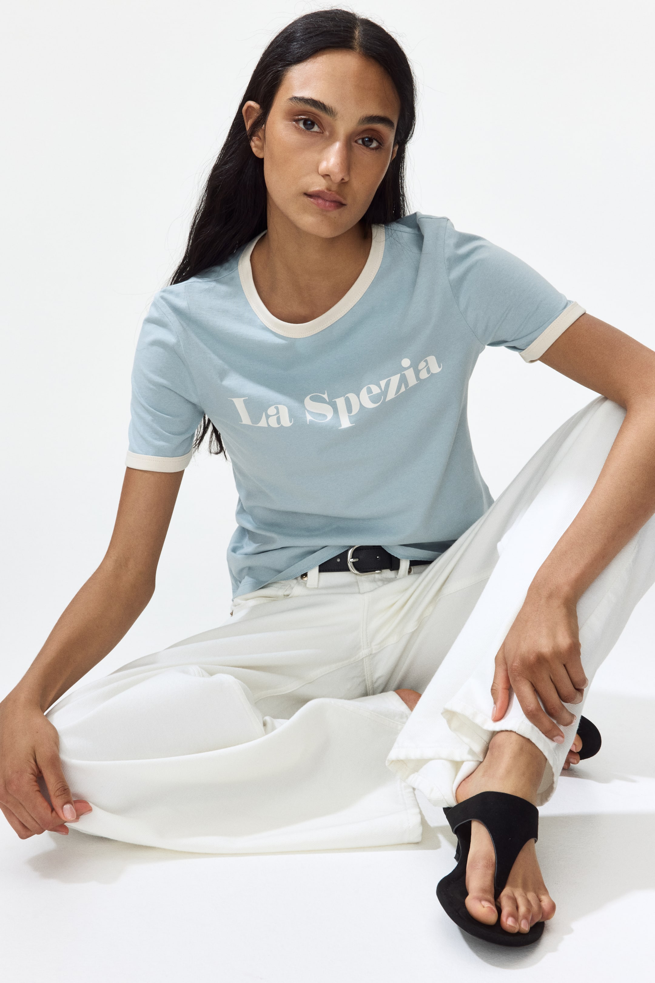 View larger image: A light blue T-shirt features a white 'La Spezia' print motif prominently on its front. It is crafted with a round neckline and short sleeves, each adorned with narrow, contrasting off-white trims.