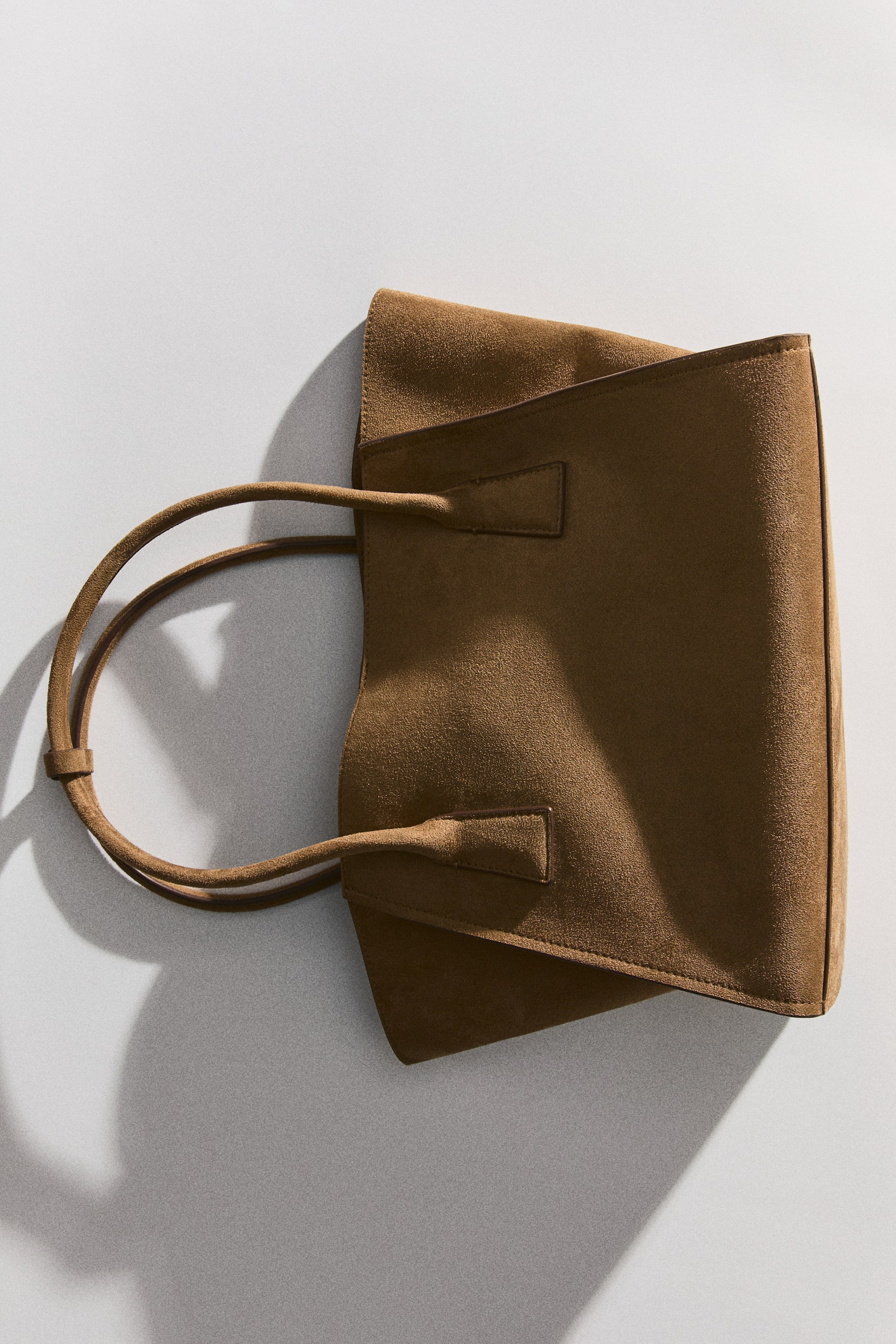 View larger image: A small shopper bag is shown with its brown, textured material and tubular handles. The handles are being fastened together with a tab.