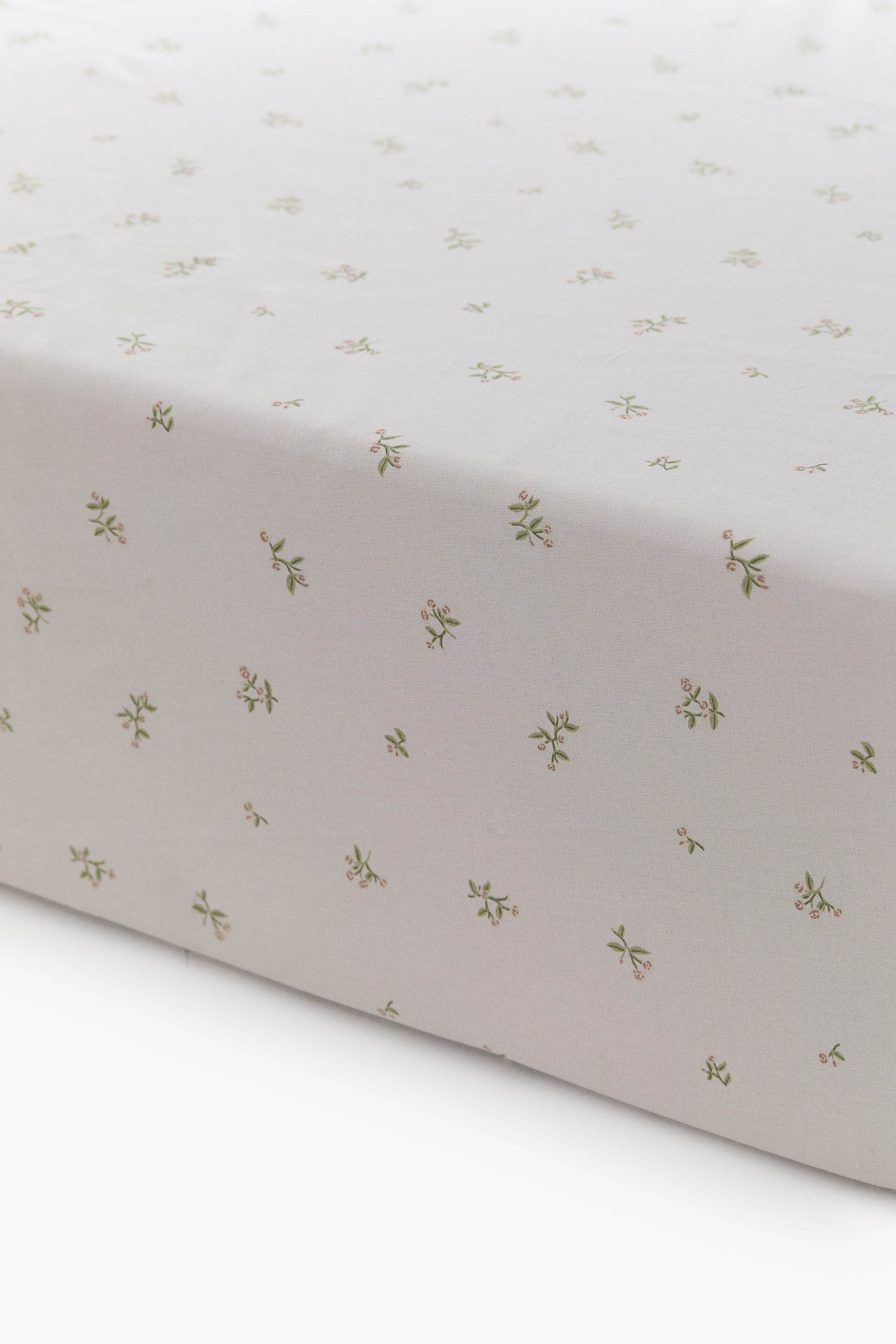 View larger image: A fitted sheet showcases a light neutral patterned cotton weave adorned with delicate green stems and pink berries. It envelops a surface, with its side visible, illustrating its snug fit.