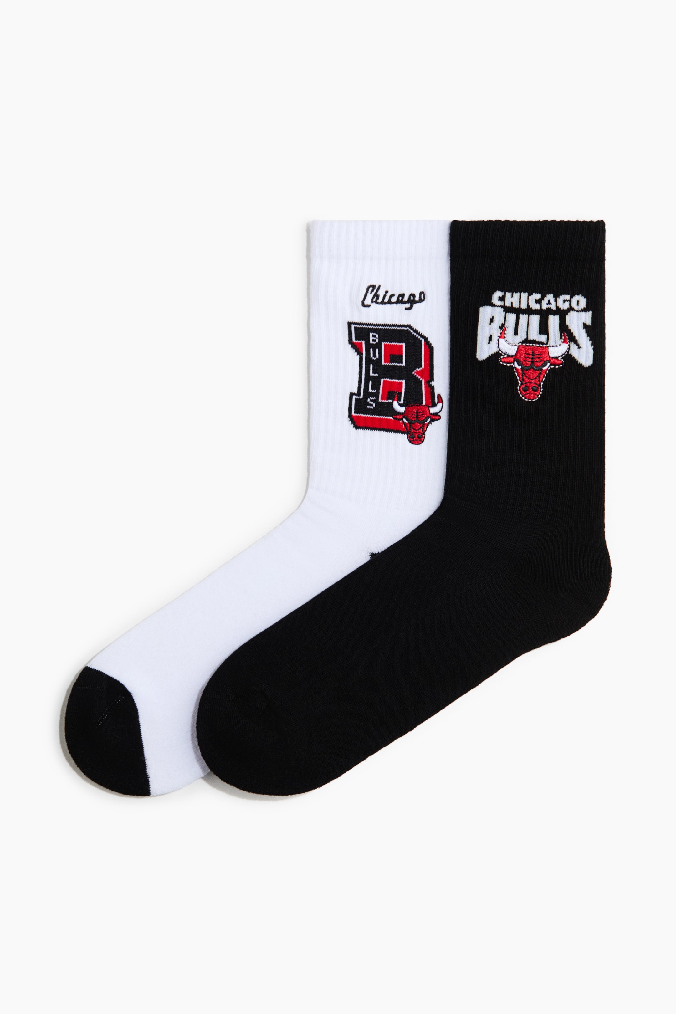 Visualizza l'immagine ingrandita: Un paio di calze morbide in misto cotone a maglia fine è posizionato frontalmente. La calza bianca presenta il logo "B" rosso e nero dei Chicago Bulls con il testo "Chicago", mentre la calza nera mostra il logo rosso e bianco dei Chicago Bulls e il testo "CHICAGO BULLS". Entrambe le calze hanno gambali alti e a coste.