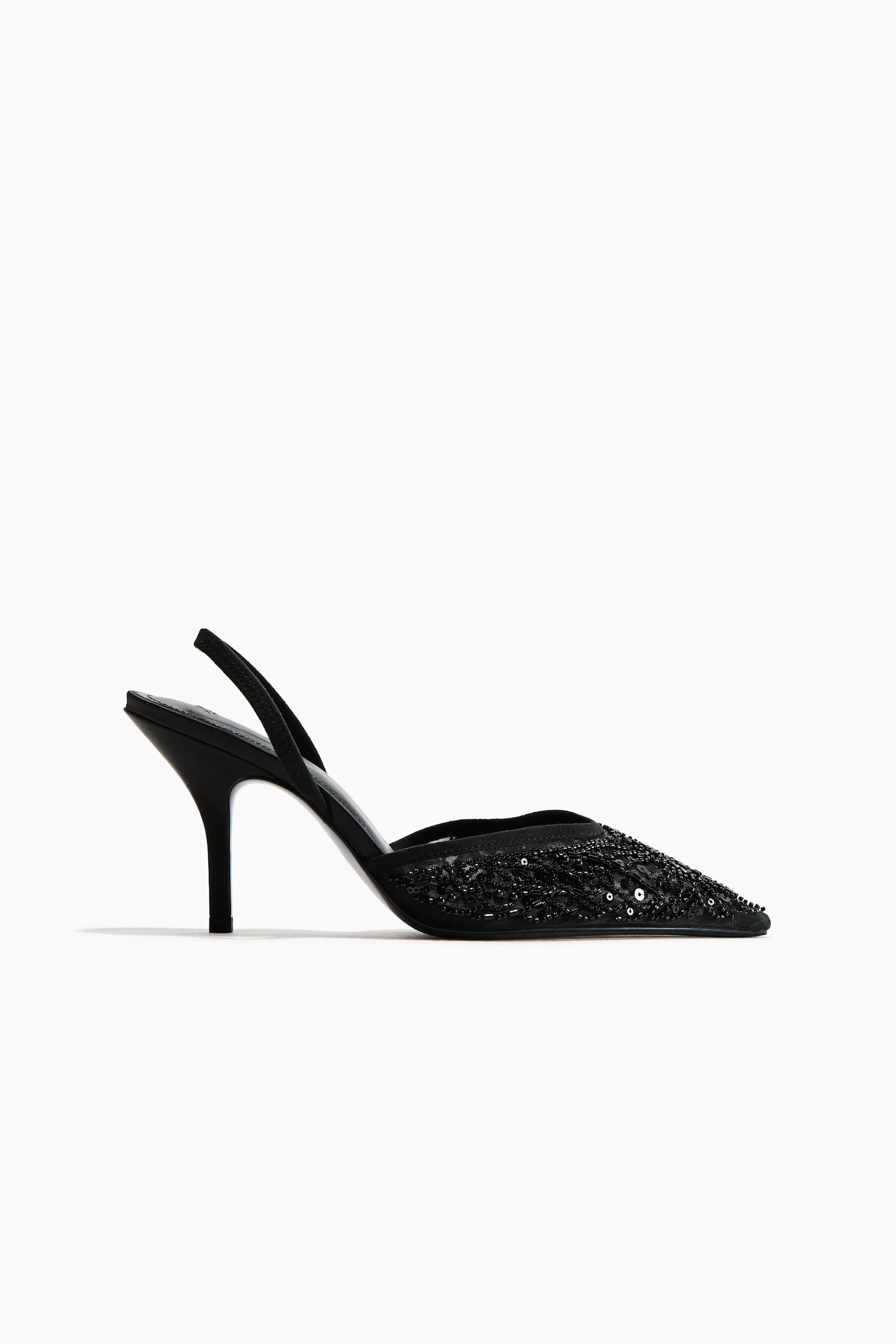 A black slingback shoe is shown in a side profile facing right, featuring a pointed toe embellished with intricate black beadwork and sequins. The shoe features a semi-sheer mesh upper, a slender stiletto heel, and a thin back strap.
