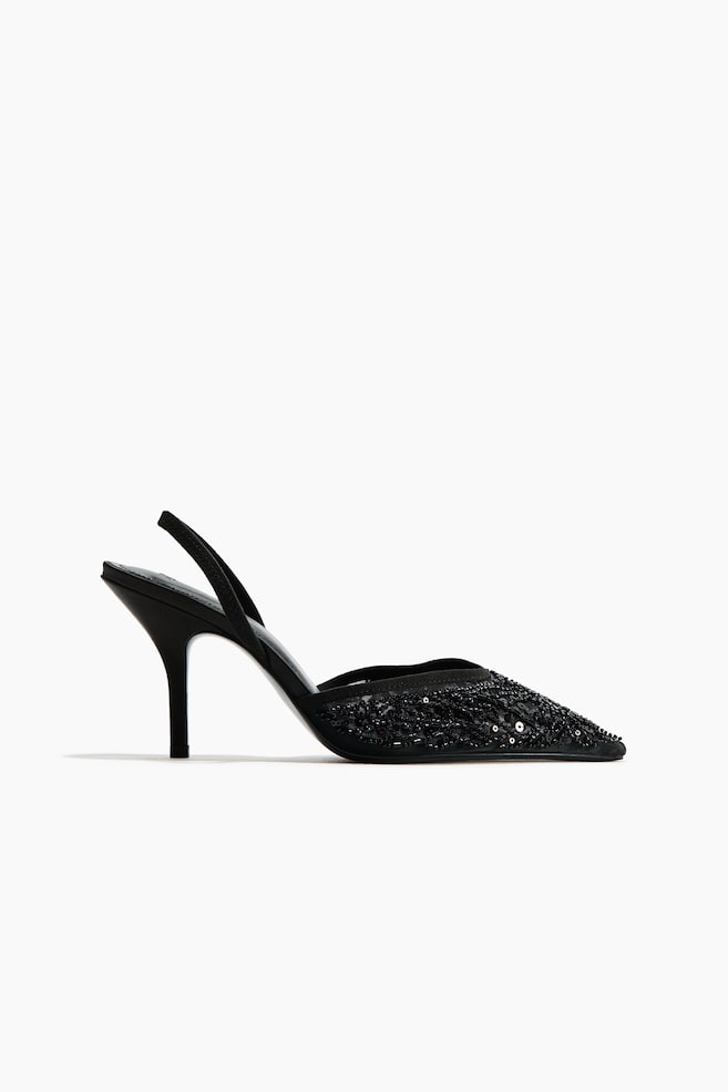 A black slingback shoe is shown in a side profile facing right, featuring a pointed toe embellished with intricate black beadwork and sequins. The shoe is displaying a semi-sheer mesh upper, a slender stiletto heel, and a thin back strap. - 1