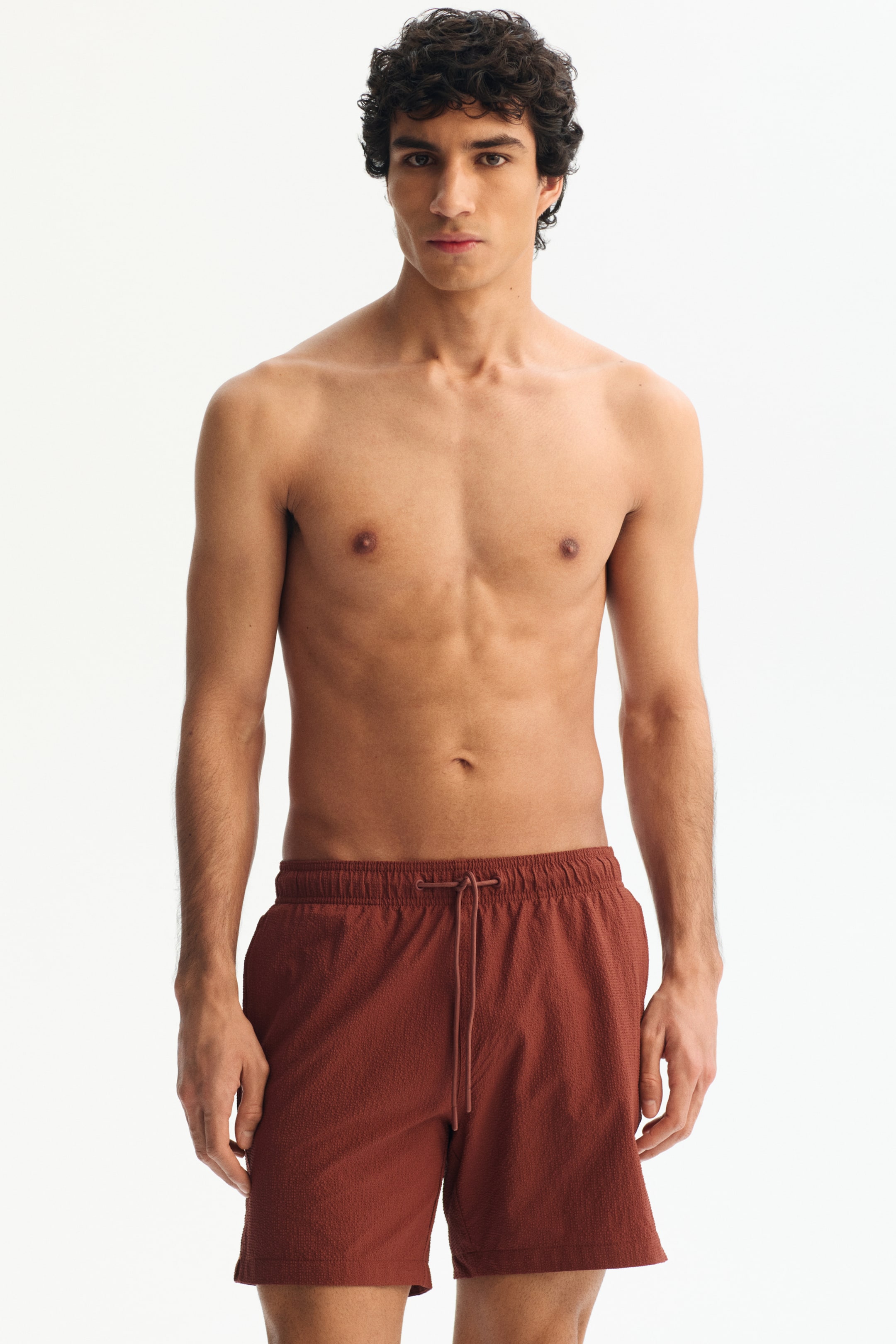 View larger image: Burnt orange crinkled textured shorts featuring a relaxed fit, an elastic waistband with a matching drawstring, and side pockets, reaching mid-thigh length.