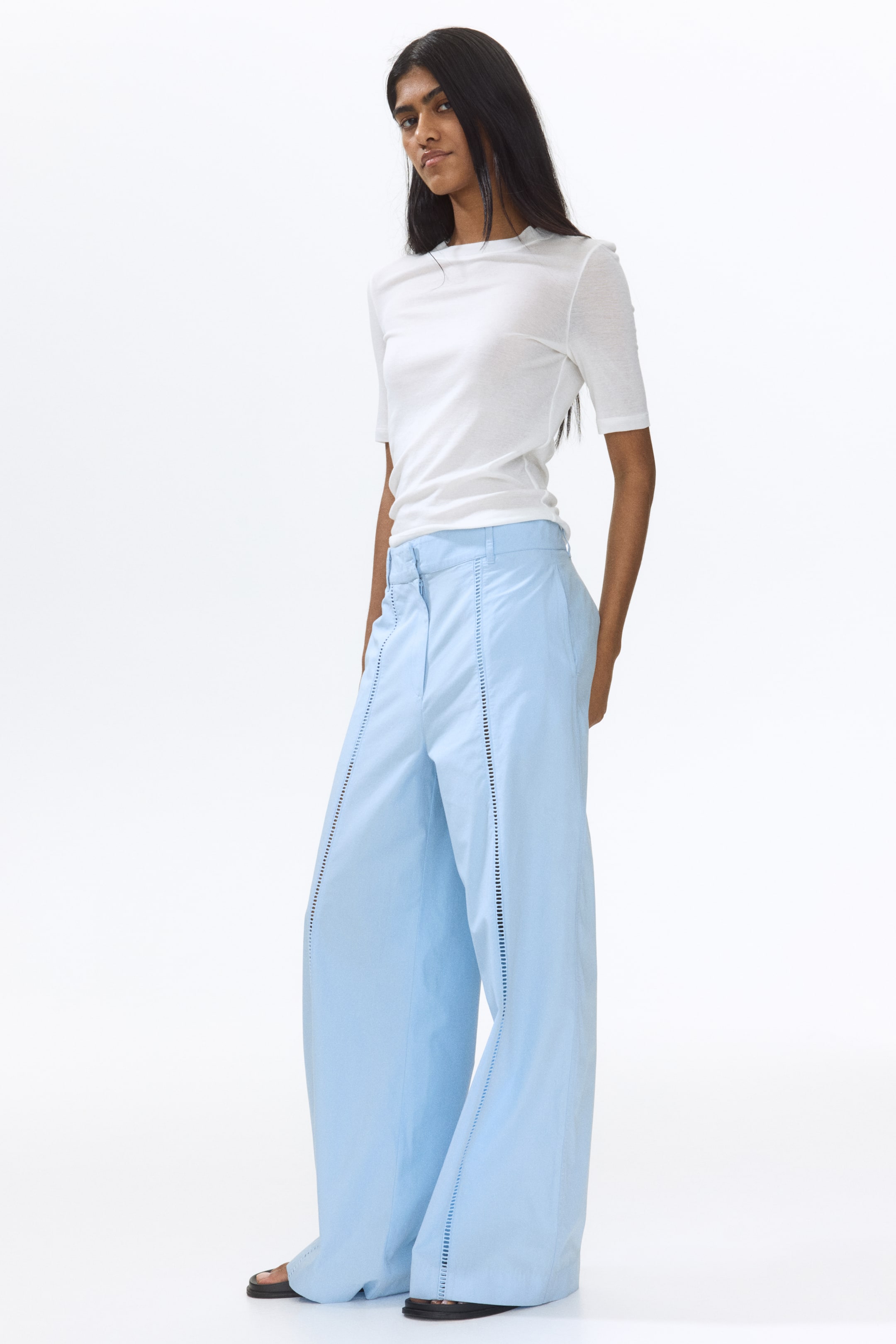 View larger image: The model is wearing light blue trousers crafted in a crisp weave, showcasing wide legs adorned with ladder lace insets along the front and subtle side pockets. The model is in a standing pose.
