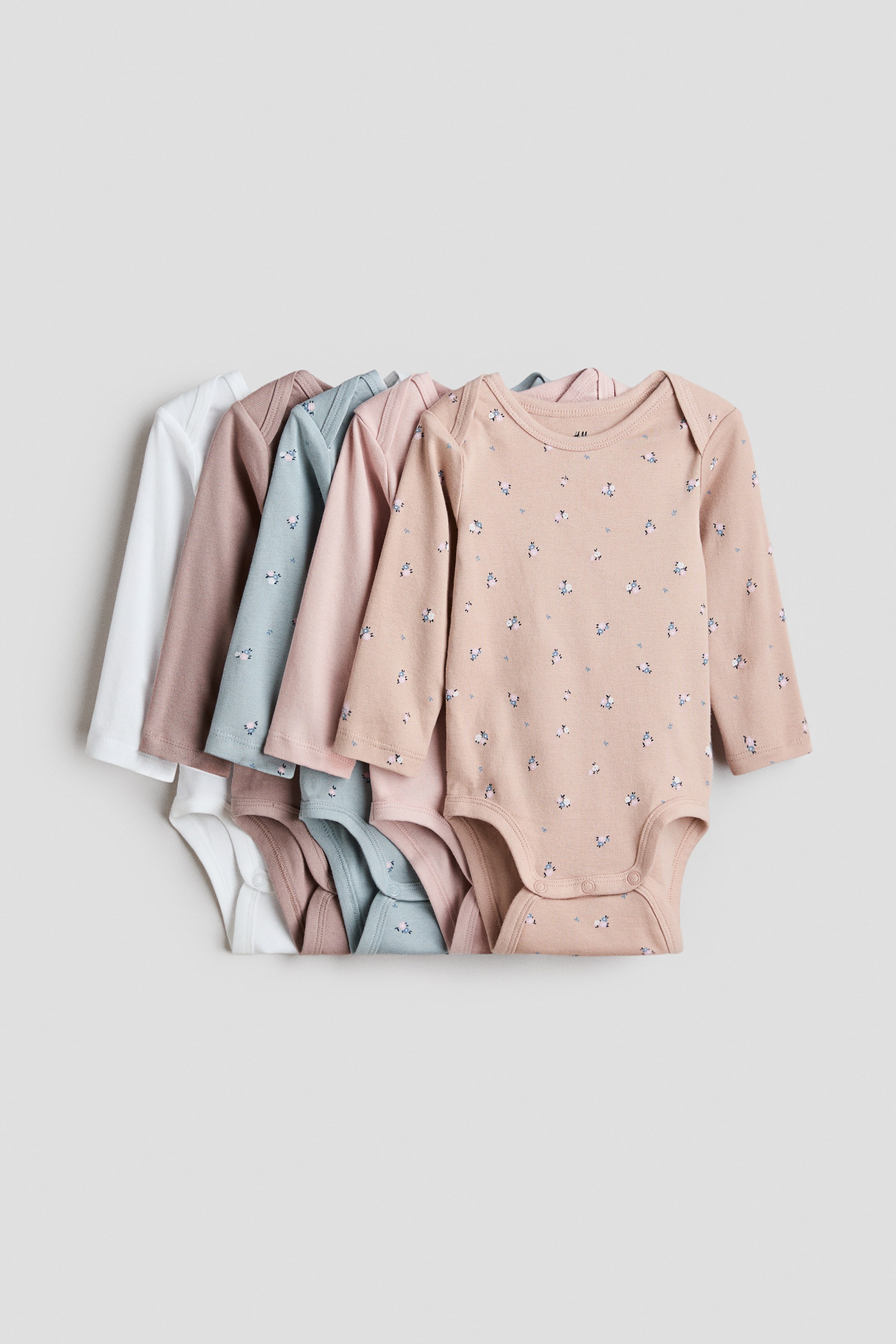 View larger image: Long-sleeved bodysuits are spread out, displaying their front views. They feature envelope necklines and press-studs at the bottom, and come in solid white, muted brown, and light pink, with two patterned bodysuits in light blue and peach.