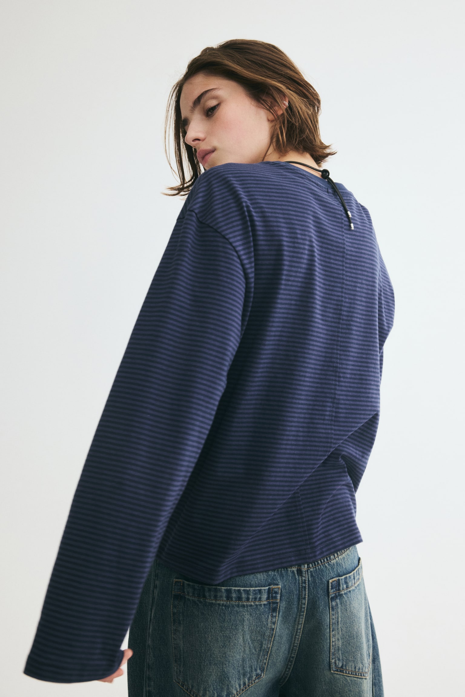 A dark blue long-sleeved shirt is laid out flat, showcasing thin horizontal stripes in two shades of blue. It boasts a crew neck, wide, relaxed-fit long sleeves, and a straight hem. - 1