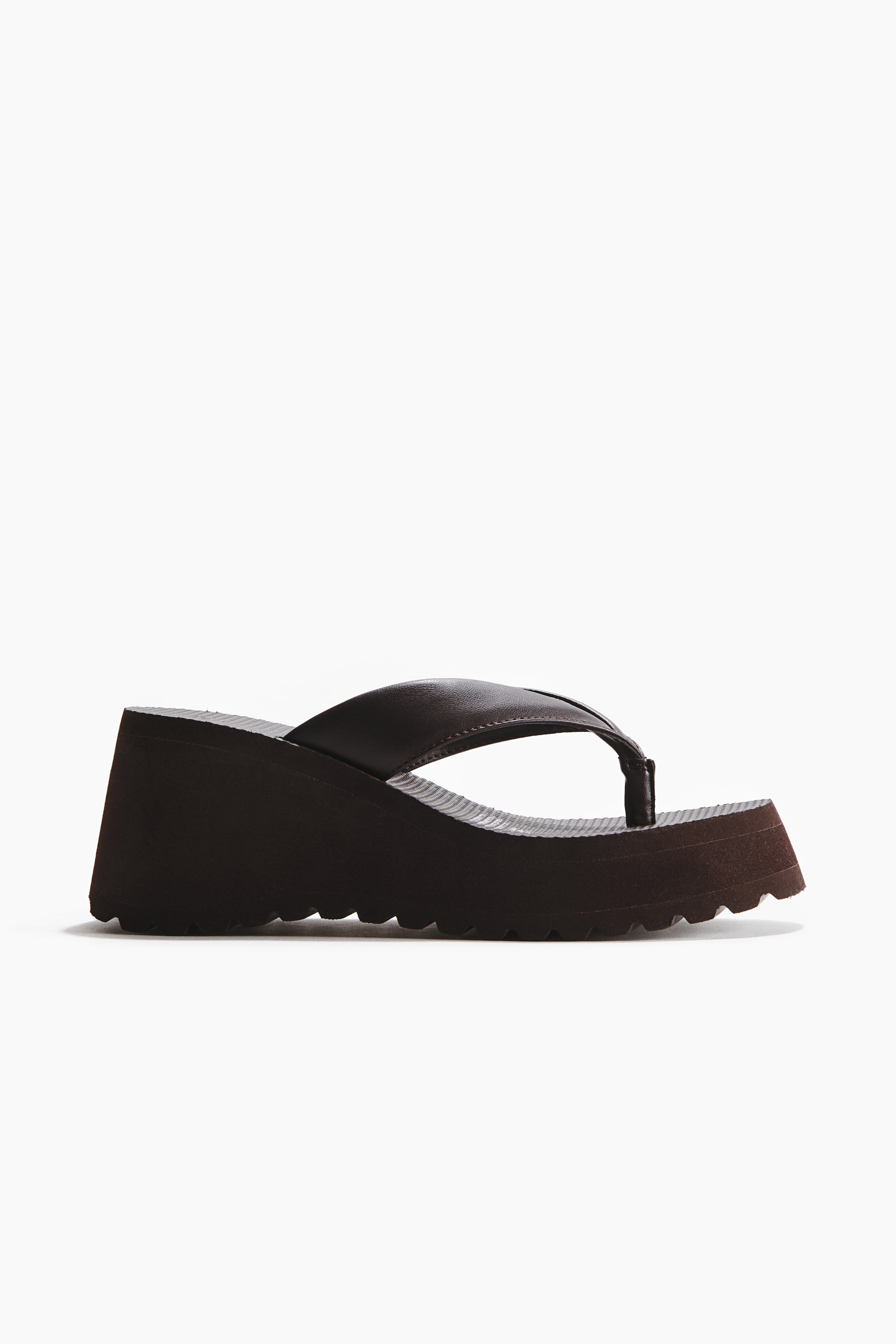 Grotere afbeelding bekijken: Een donkerbruine wedge teenslipper met een gladde teensluiting en een dikke, donkerbruine platformschoenzool met een opvallend golvend profiel. Het voetbed heeft een geribbelde textuur.