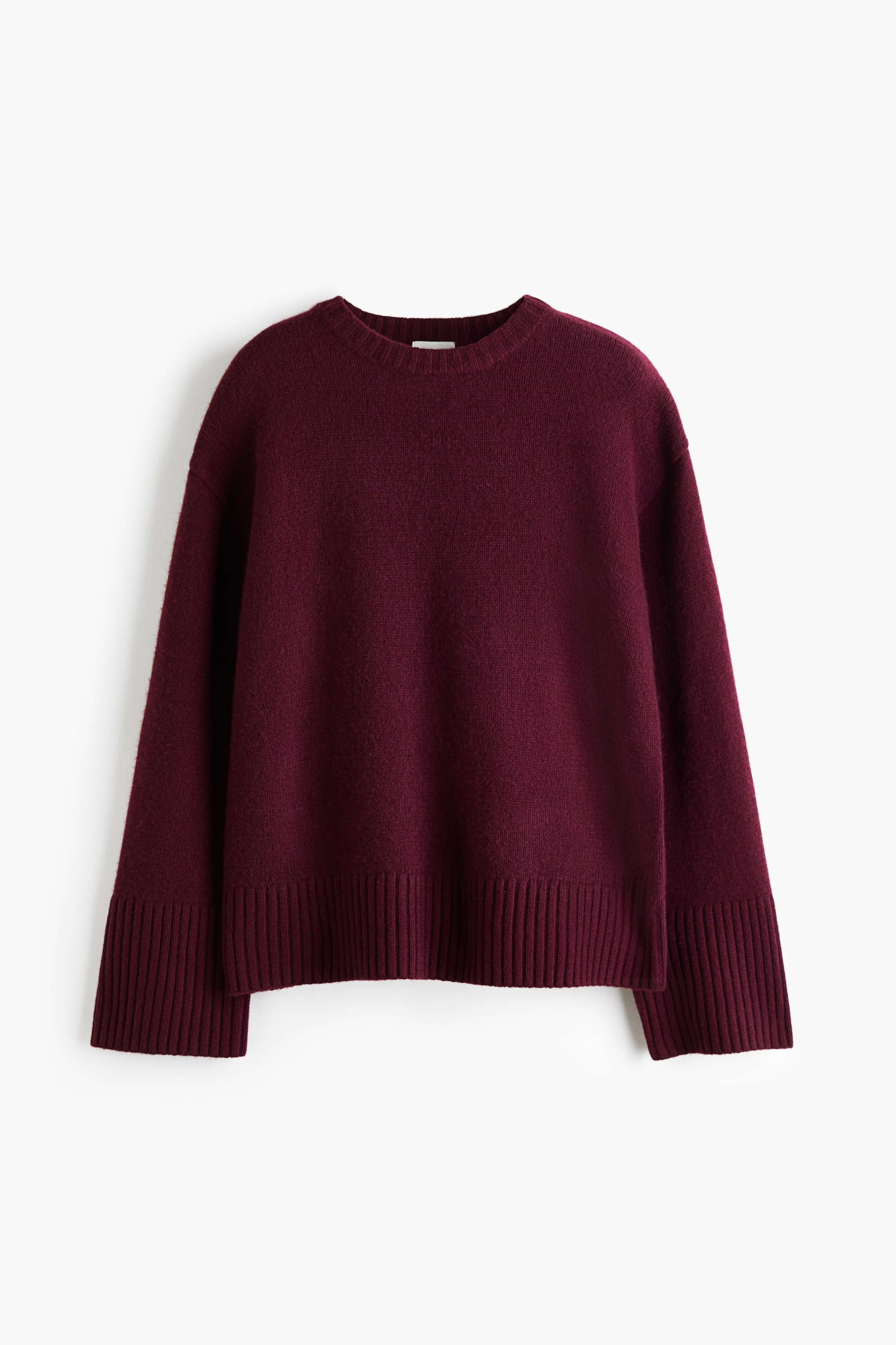 View larger image: An oversized burgundy knit sweater is shown from the front, showcasing dropped shoulders and long, wide sleeves. The sweater features a ribbed crew neck, wide ribbed cuffs, and a ribbed hem.