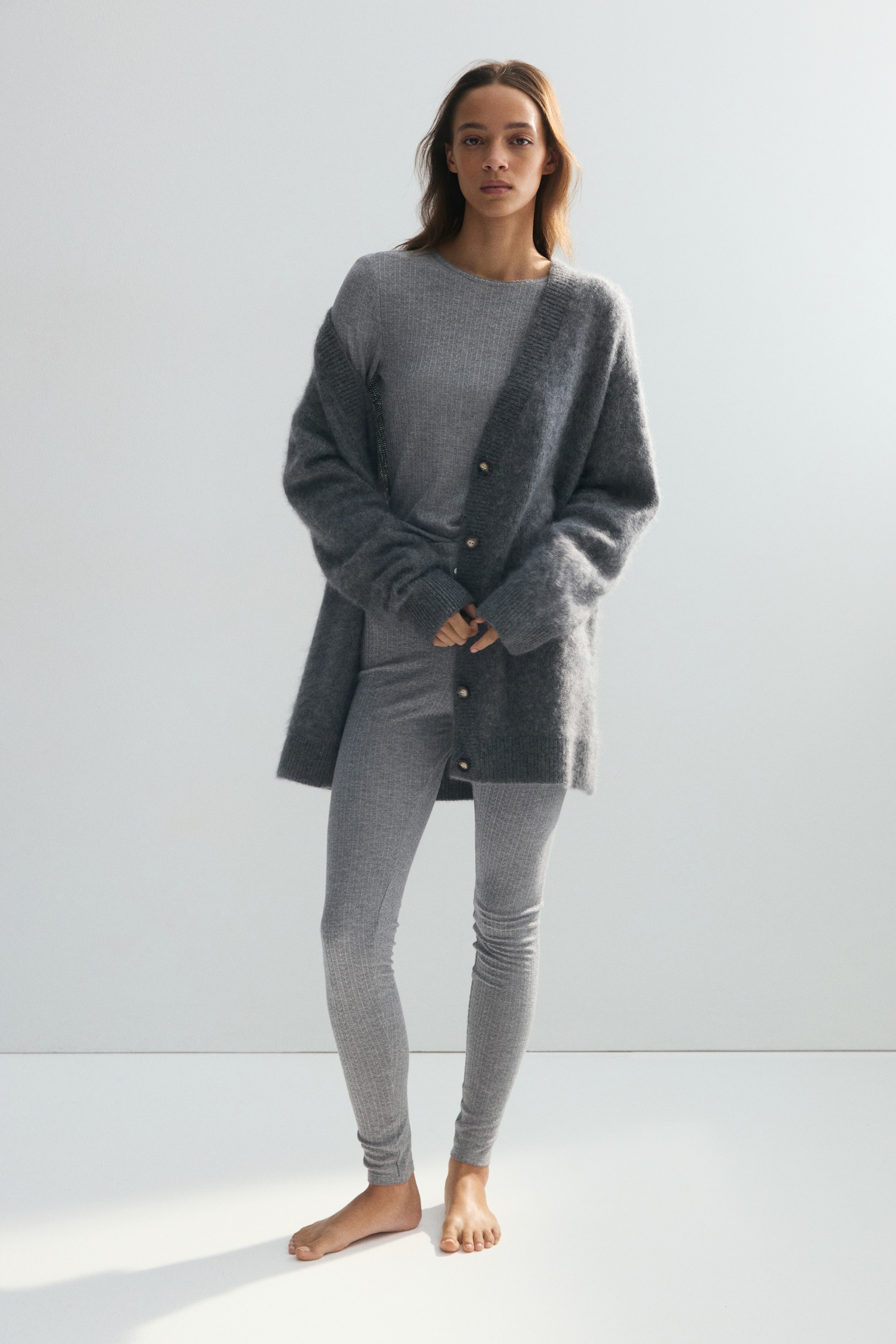 A grey two-piece loungewear set, featuring a fine chevron ribbed knit, is being displayed from the front, including a long-sleeved crew neck top and matching full-length slim-fit pants.
