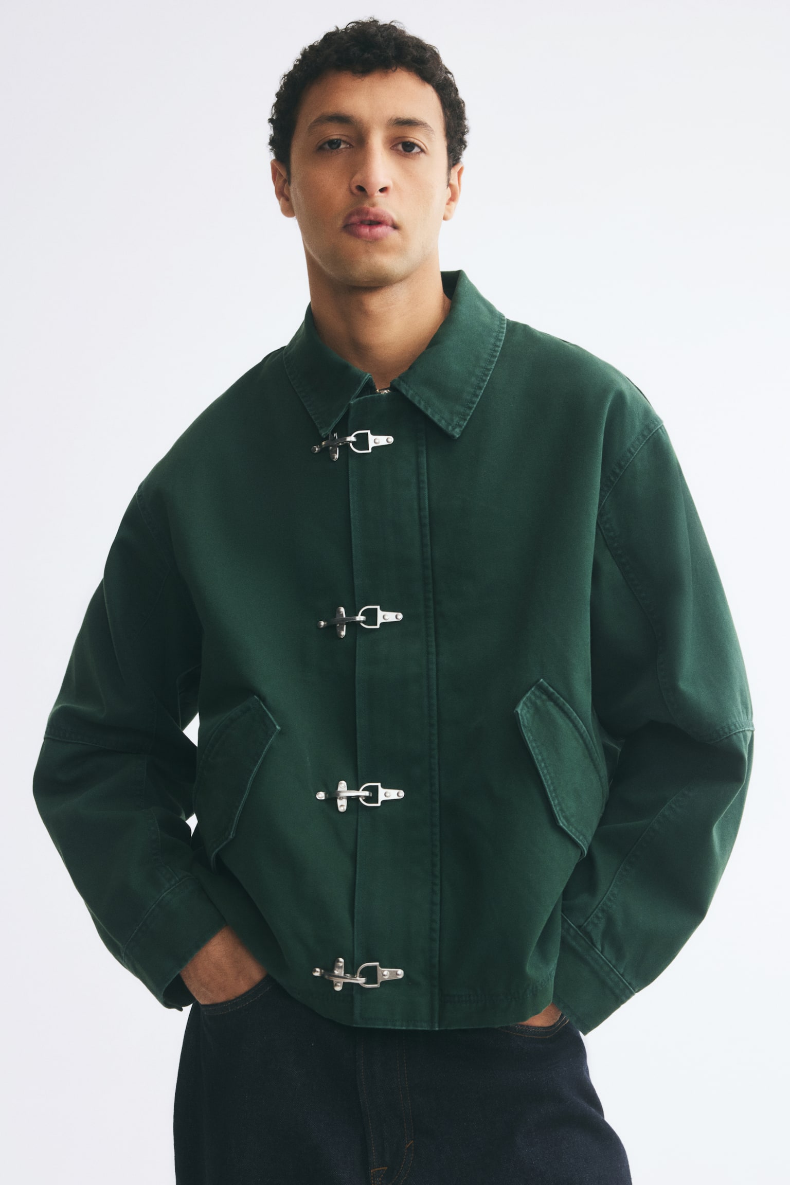 Má»t chiáº¿c Ã¡o khoÃ¡c váº£i canvas cotton mÃ u xanh lÃ¡ Äáº­m Äang ÄÆ°á»£c chá»¥p chÃ­nh diá»n, ná»i báº­t vá»i cá» Ã¡o nhá»n cá» Äiá»n, vai xuÃ´i vÃ  náº¹p chá»ng giÃ³ phÃ­a trÆ°á»c ÄÆ°á»£c cá» Äá»nh báº±ng bá»n khÃ³a kim loáº¡i mÃ u báº¡c. Ão khoÃ¡c cÃ³ hai tÃºi viá»n xÃ©o phÃ­a trÆ°á»c vá»i náº¯p tÃºi nhá»n. - 1