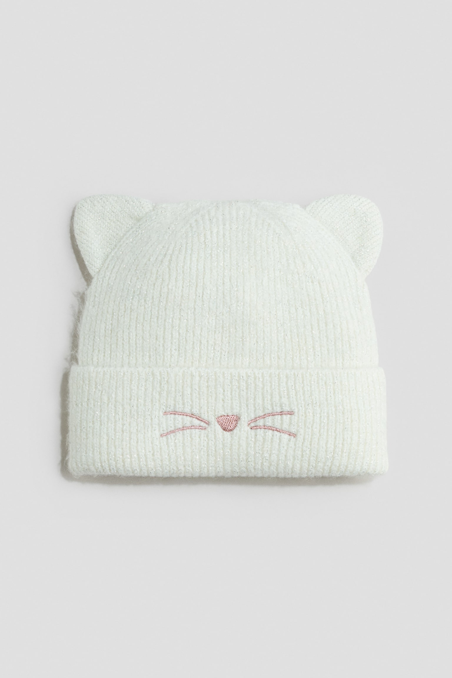 Eine weiÃe, gerippte StrickmÃ¼tze ist frontal ausgerichtet und verfÃ¼gt Ã¼ber zwei gestrickte Katzenohren auf der Krone sowie einen breiten, umgeschlagenen Bund. Auf dem Bund ist mittig eine kleine, rosa gestickte Katzennase mit Schnurrhaaren zu sehen.