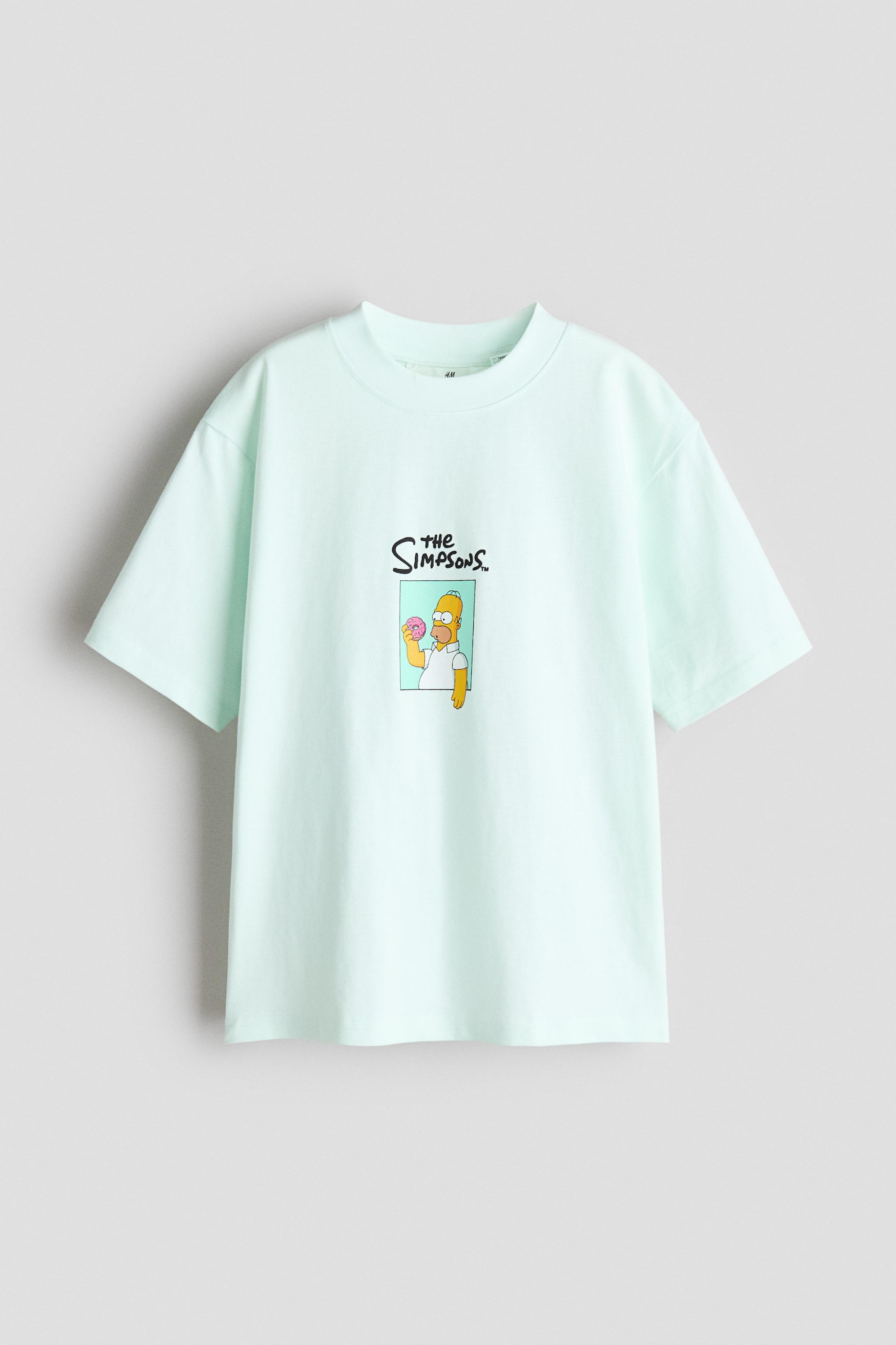 Größeres Bild anzeigen: Ein hellgrünes T-Shirt aus weichem, gemustertem Baumwolljersey wird von vorne präsentiert und verfügt über einen gerippten Besatz am Halsausschnitt. Es zeigt eine Grafik von Homer Simpson, der einen Donut hält, mit dem Text "the SIMPSONS" darüber und bietet eine lockere Passform mit überschnittenen Schultern.
