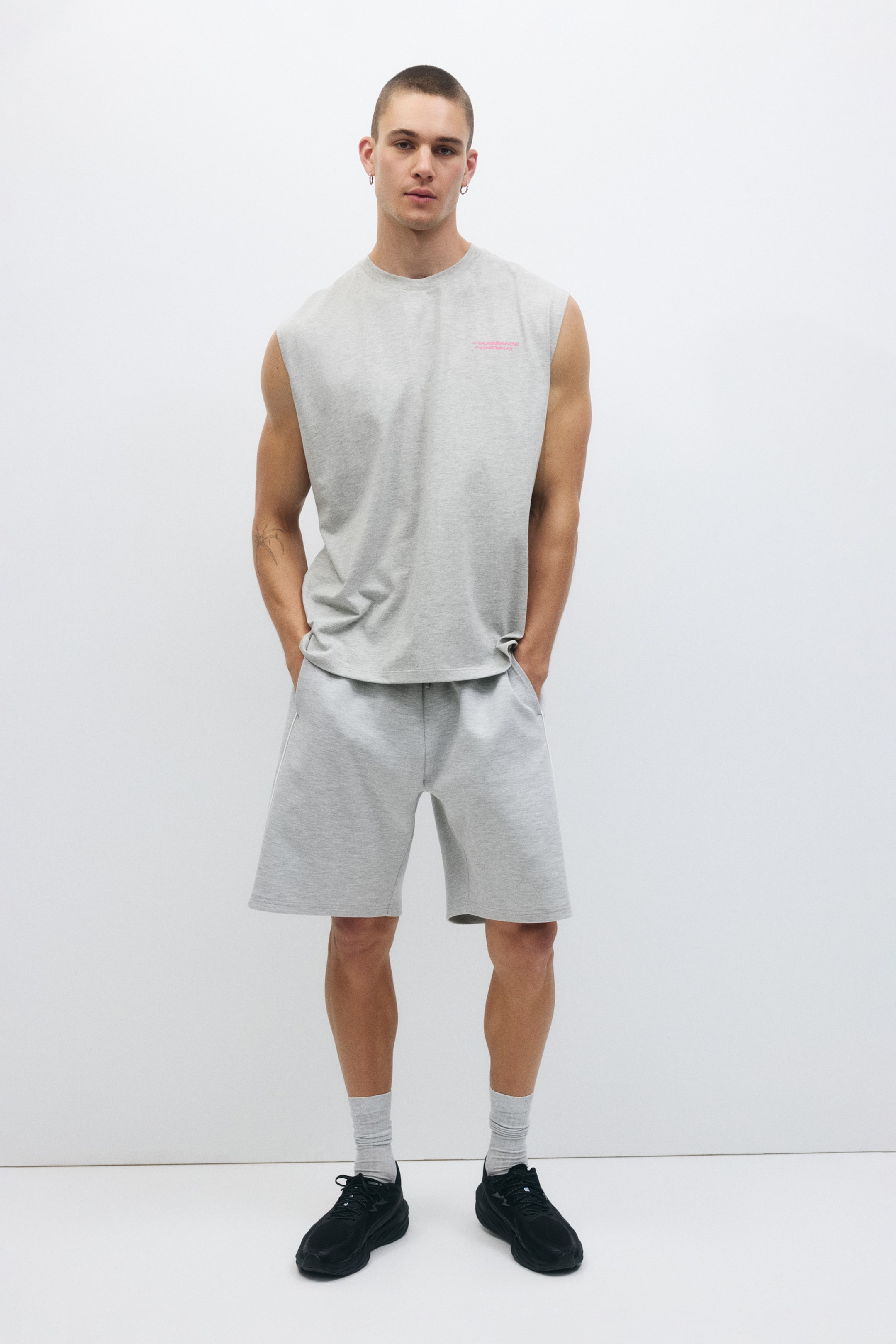 View larger image: The loose-fit sports vest top is showcased from the front in a light gray marl. It features a crew neck, wide armholes, and a straight hem, with a small pink text logo visible on the left chest.