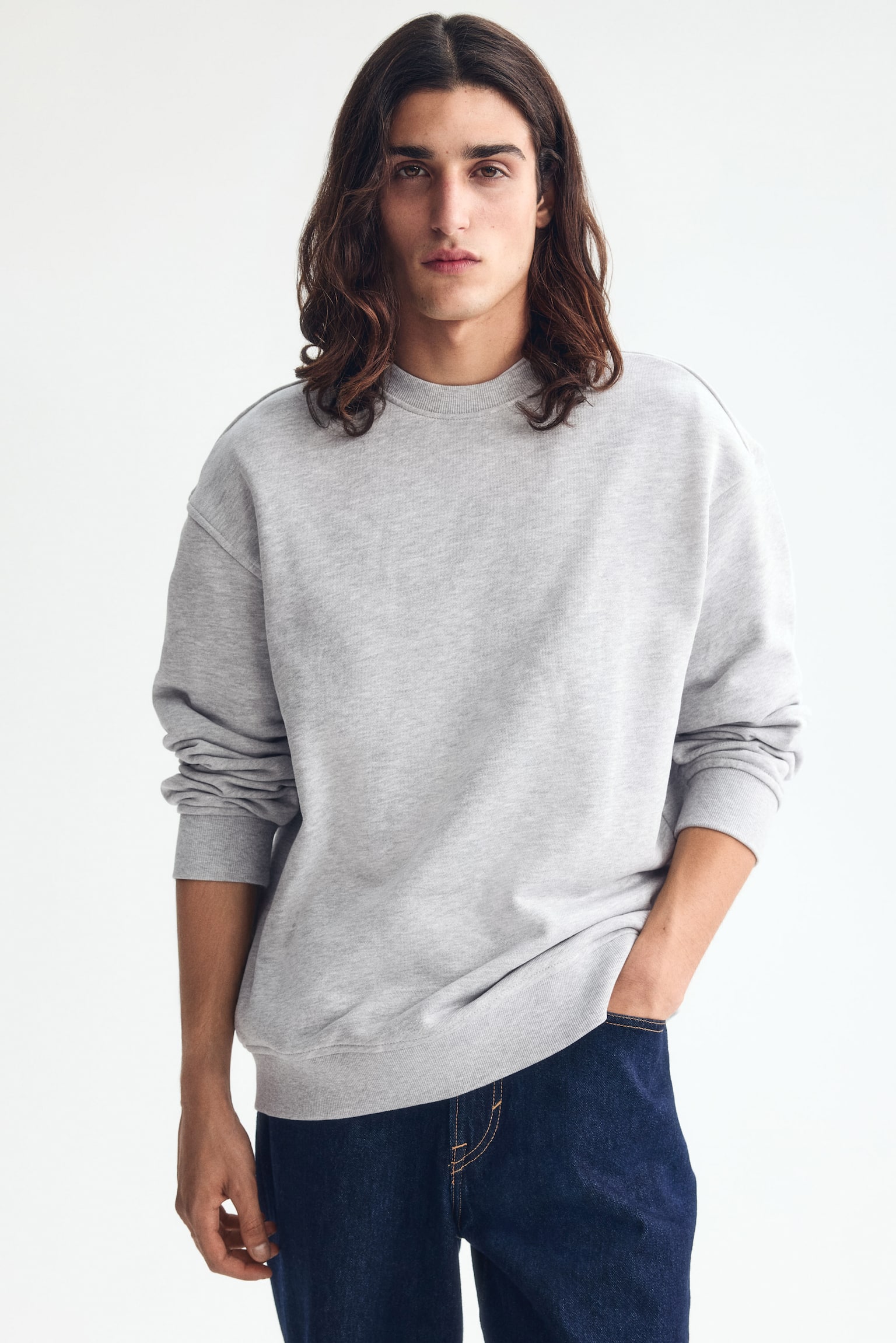 Áo sweatshirt màu xám nhạt đang thể hiện dáng rộng thoải mái từ phía trước, nổi bật với cổ tròn viền gân, vai thả và tay dài với cổ tay và gấu áo rộng có gân. - 1
