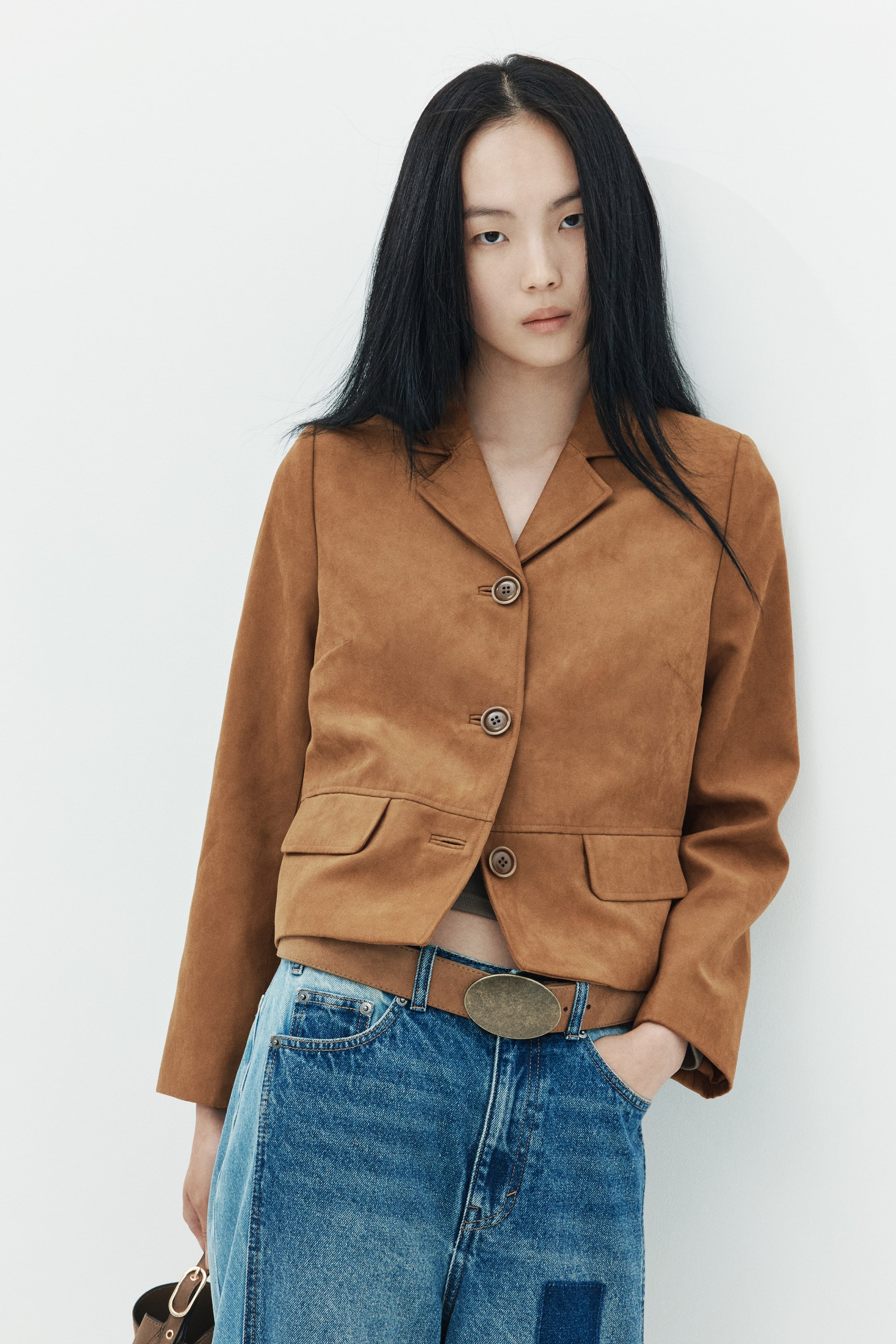 View larger image: A brown single-breasted blazer in a woven fabric is worn by the model, buttoned up at the front. The blazer features notch lapels and mock flap pockets, and is styled with blue jeans and a brown belt.