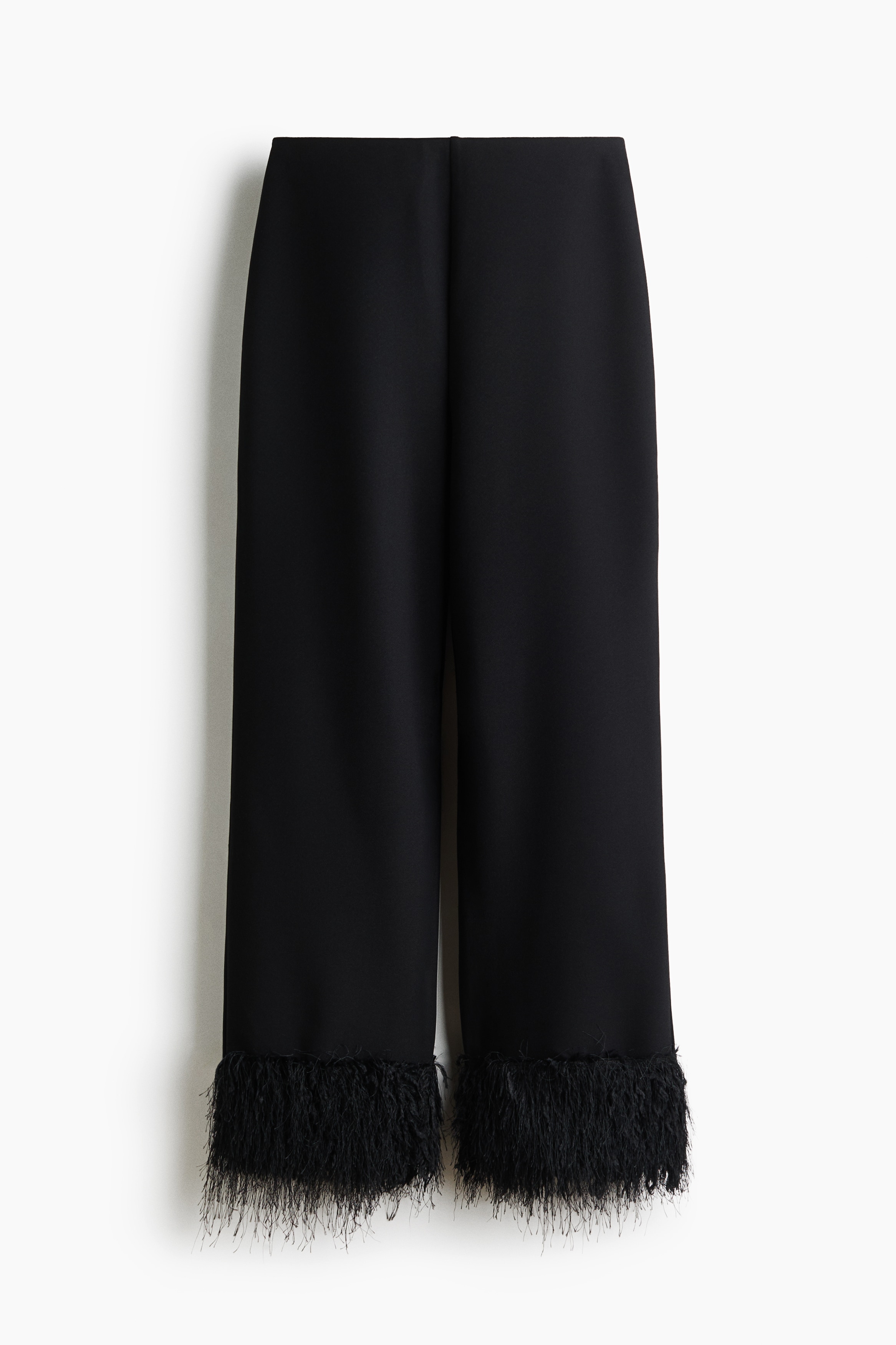 Relaxed-fit trousers in black stretch crêpe jersey are being worn by the model, featuring straight legs finished with dense sequinned fringe at the hems. The trousers are being styled with a matching black sleeveless top with a fringed hem and black pointed-toe heeled shoes.