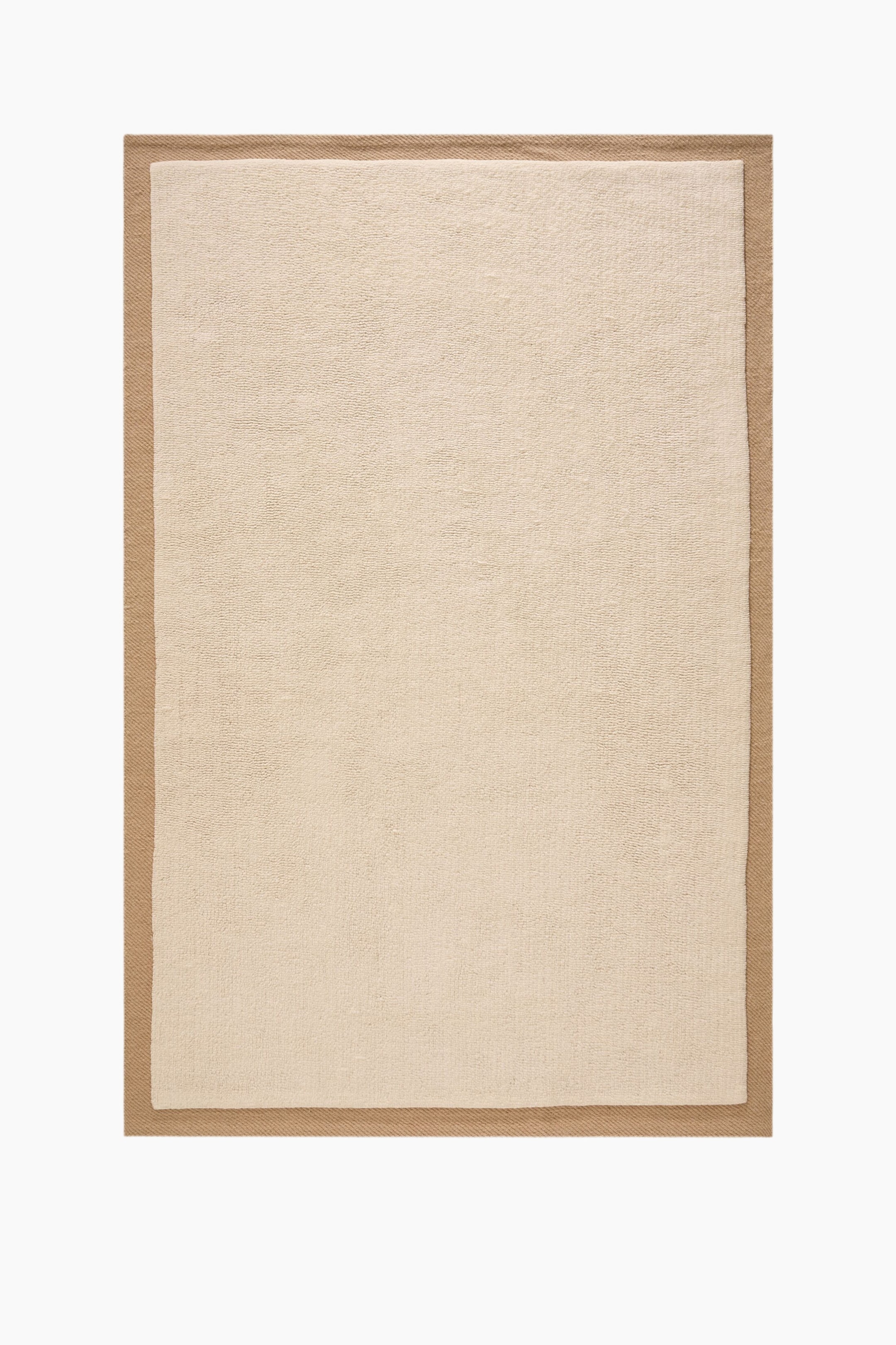Agrandir l'image: Un tapis rectangulaire présentant un panneau central beige clair avec une texture douce et à faible épaisseur, entouré d'une bordure tissée plus large de couleur fauve exhibant un motif de tissage en diagonale.