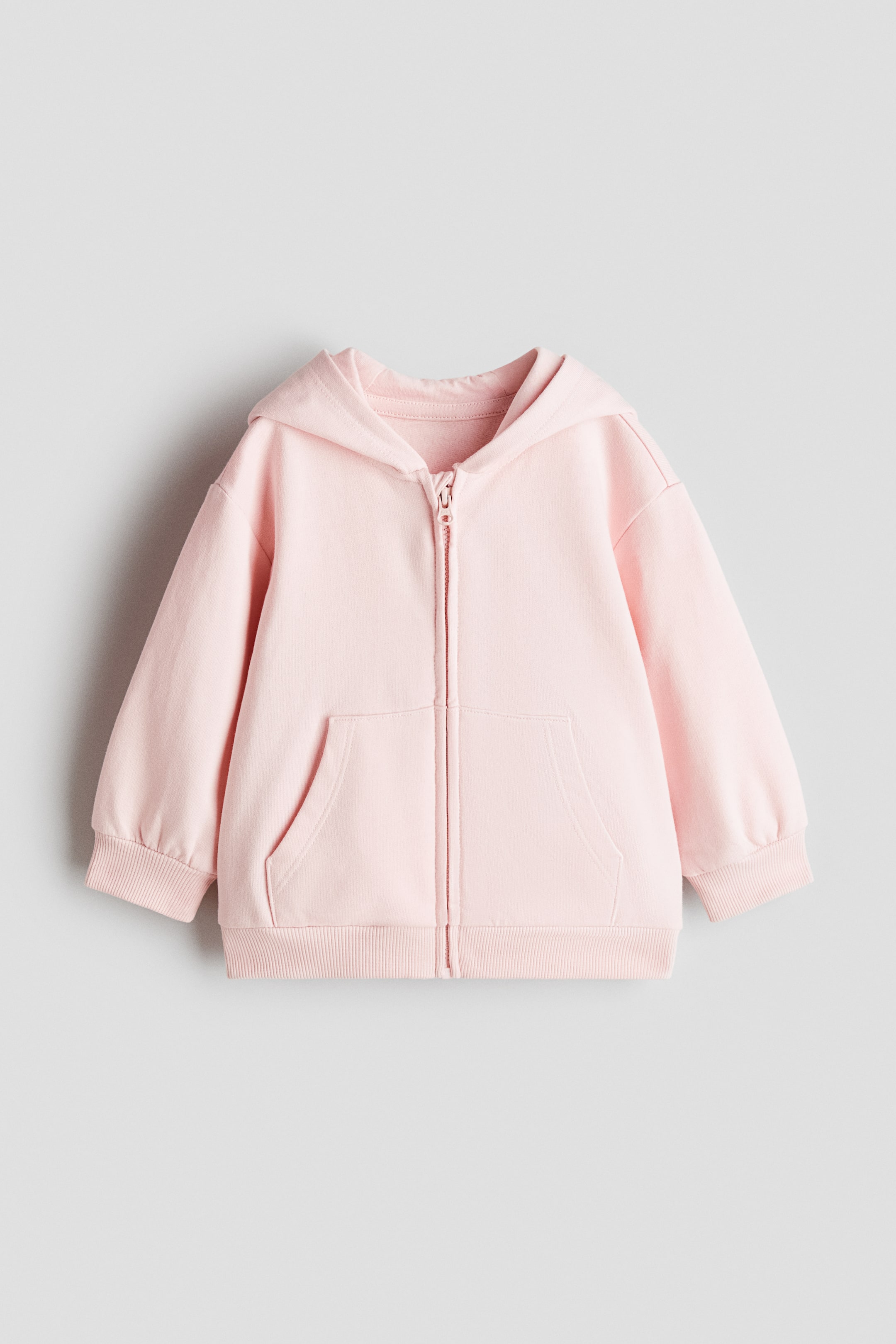 View larger image: A pink zip-through hoodie is shown from the front, featuring a lined hood, a central zip, dropped shoulders and front patch pockets. It also features ribbed cuffs and a ribbed hem.