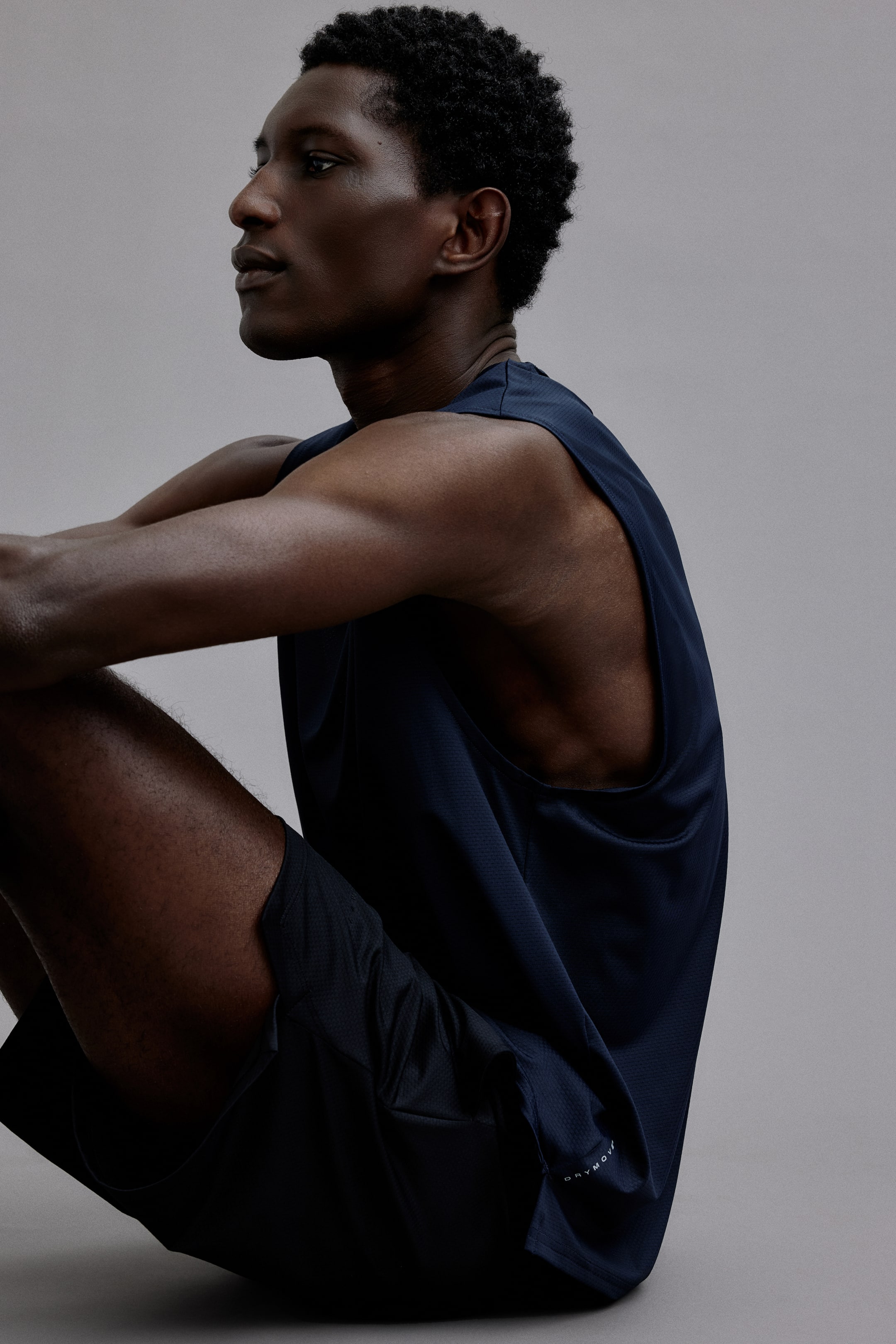 Xem ảnh lớn hơn: Bộ đồ thể thao màu xanh hải quân bao gồm áo tank top dáng rộng với cổ tròn và nách rộng, cùng quần short đồng bộ. Áo tank top có logo trắng nhỏ gần gấu áo.