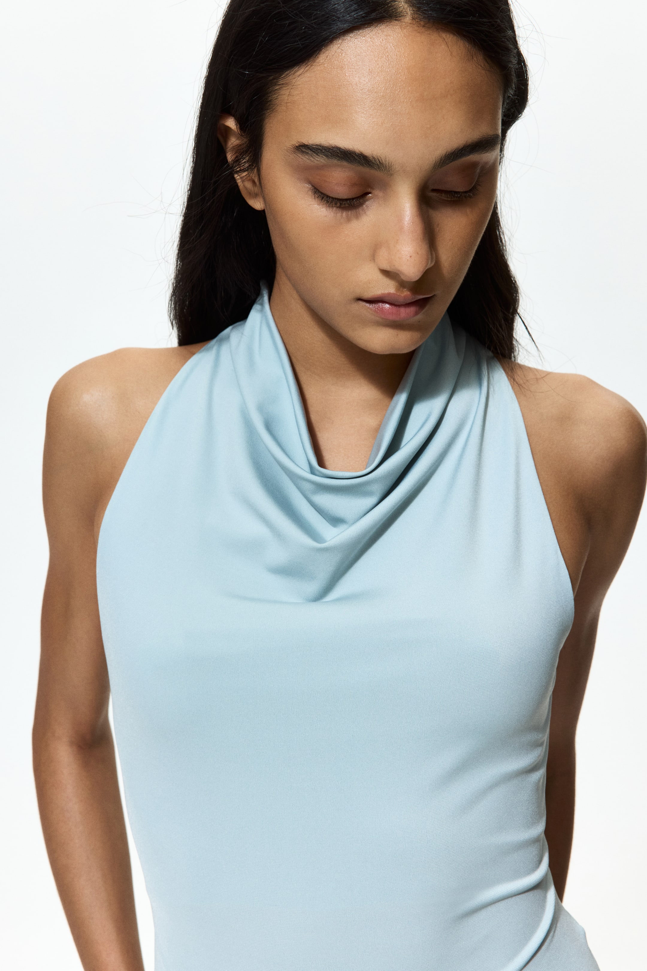 View larger image: A light blue halter-neck top featuring a draped cowl neckline, presenting a fitted silhouette on the upper body from the front.