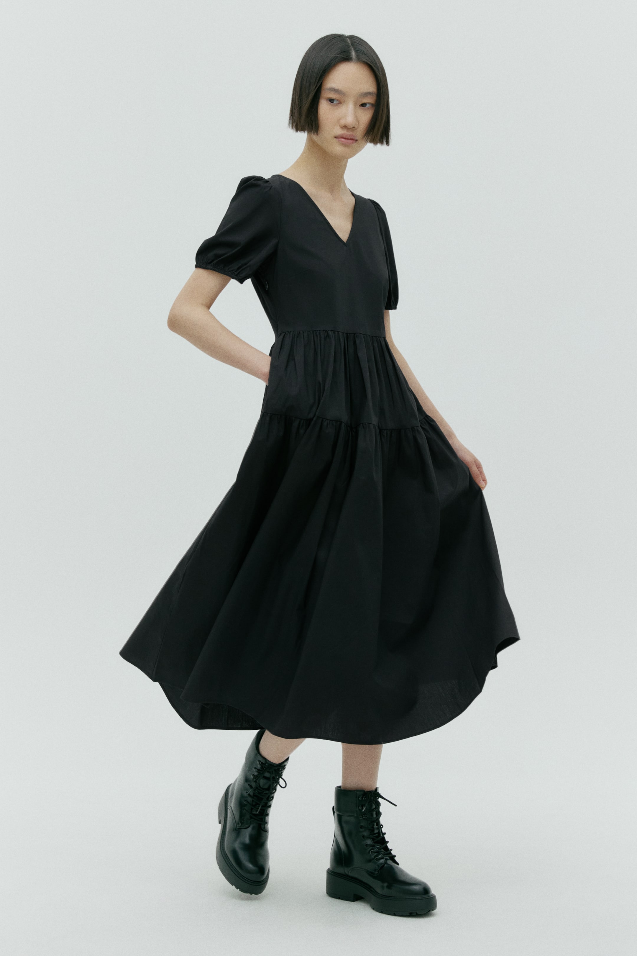 View larger image: A black midi-length dress displays a V-neckline and short puffed sleeves. The dress features a defined waistline and a tiered, flowing skirt, shown from a front-facing, slightly angled perspective.