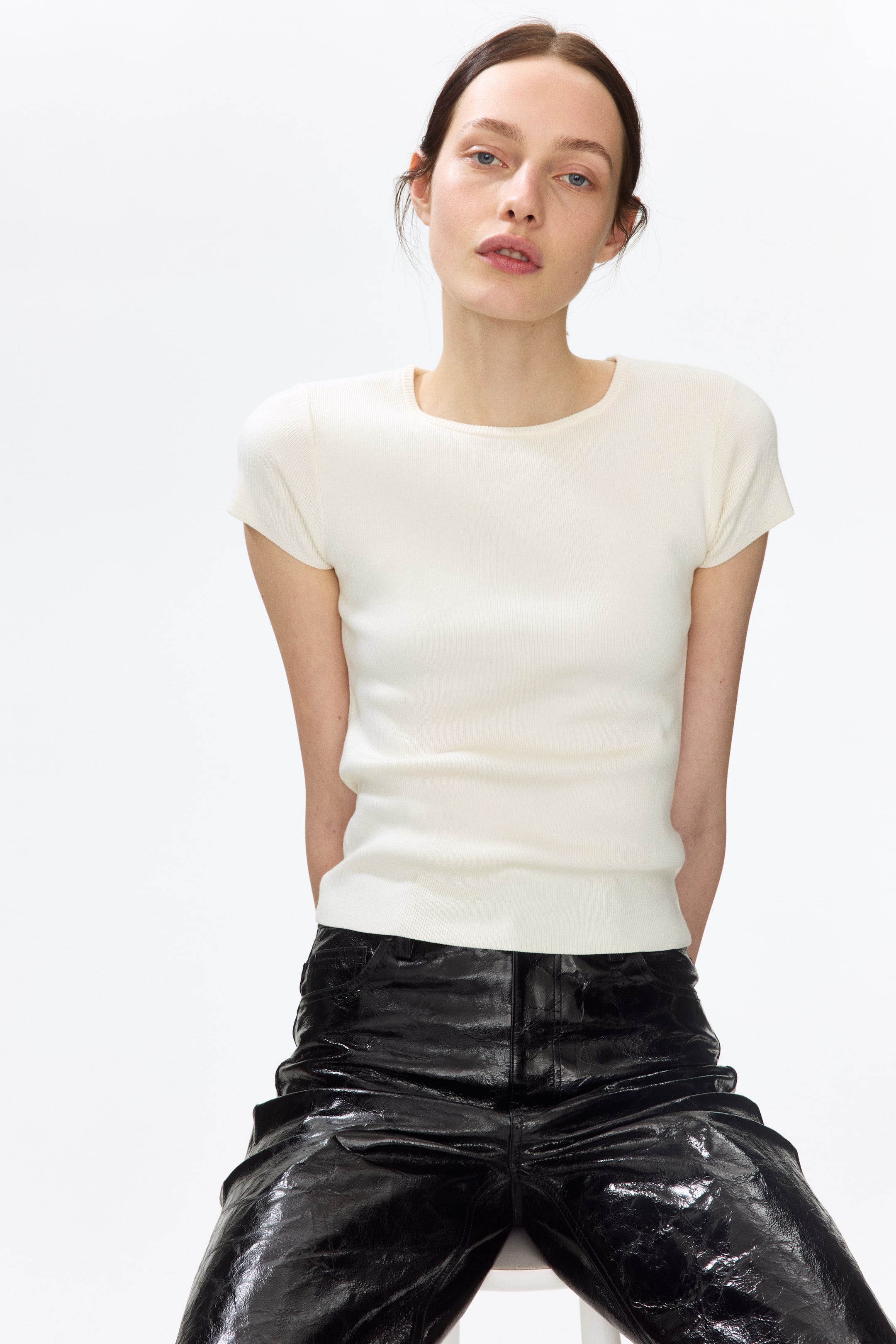 View larger image: A cream-coloured short-sleeve top featuring a ribbed knit texture and a round neckline. It fits snugly, finishing at the hip, and has short cap sleeves.