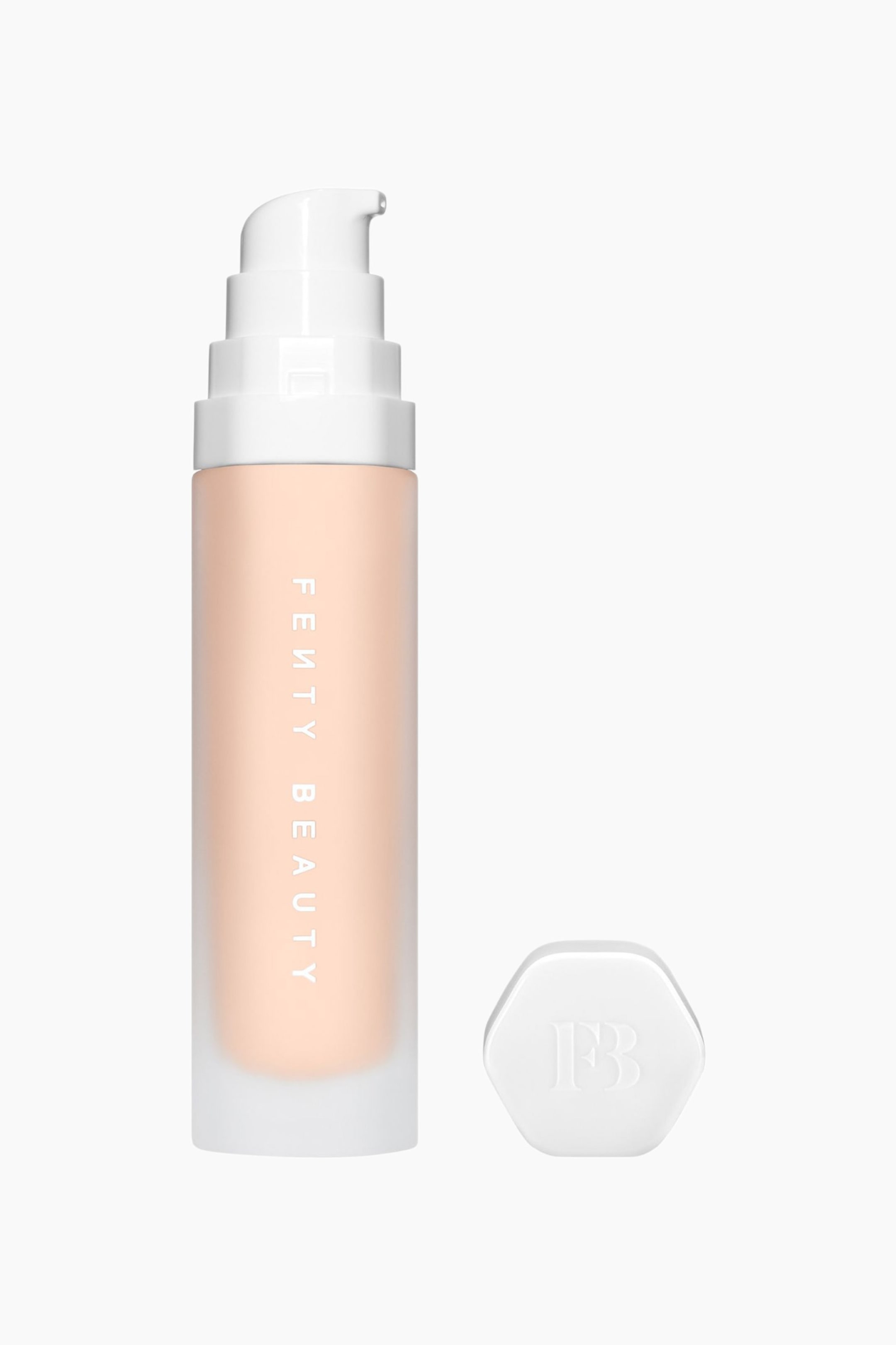 Visa större bild: Soft'lit Naturally Luminous Longwear Foundation står upprätt och visar upp en frostad cylindrisk flaska fylld med en ljus persikotonad vätska och med vertikal vit "FENTY BEAUTY"-text. En vit, nivåindelad pumpdispenser är fäst upptill, medan en separat vit sexkantig kork med en präglad "FB"-logotyp vilar bredvid flaskans bas.