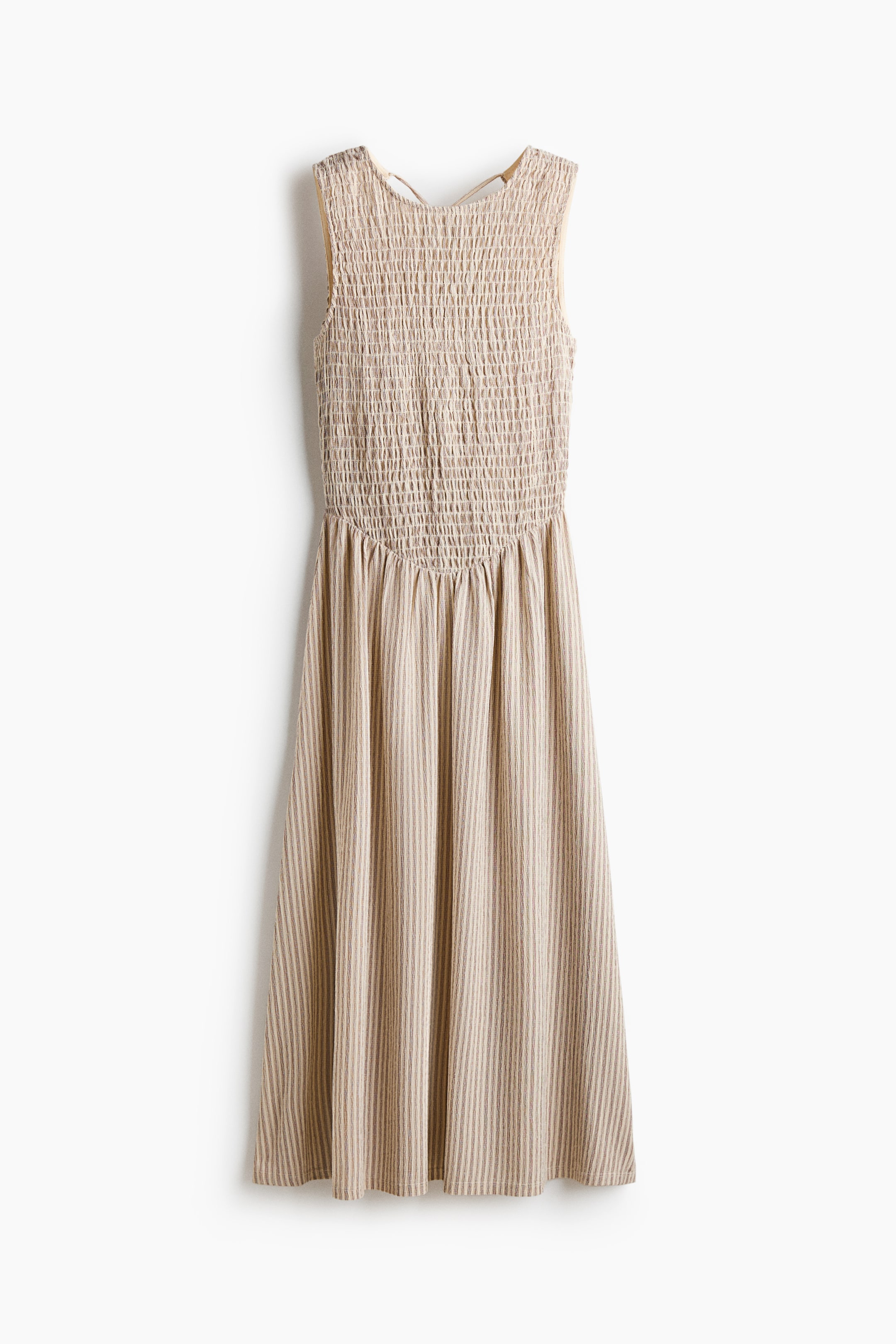 View larger image: A sleeveless dress is hanging facing front, featuring a smocked bodice in light beige. The skirt is flowing from the gathered waist, presenting vertical stripes in alternating shades of beige.