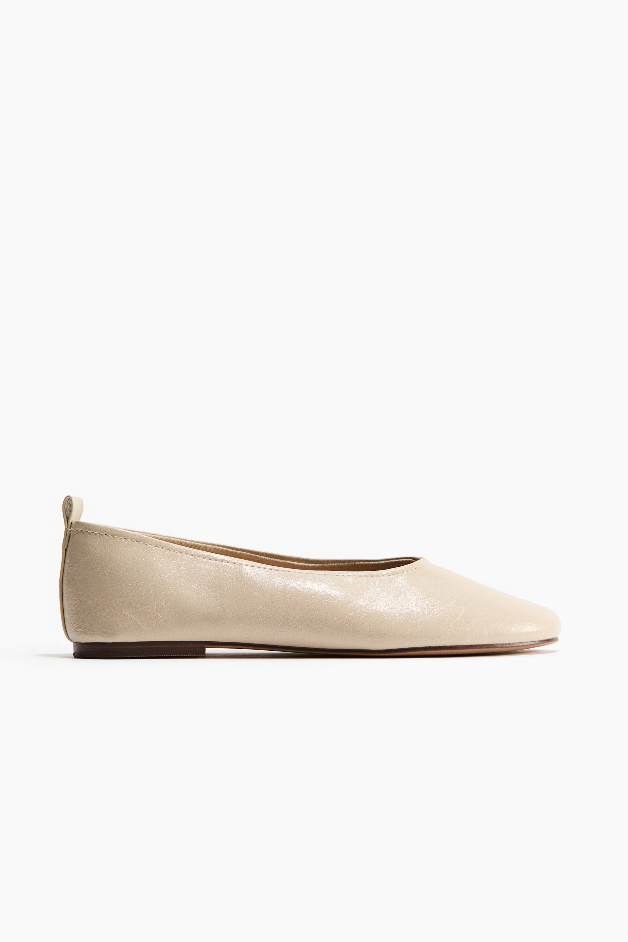 View larger image: A light beige ballet pump presents its side profile, featuring a smooth, soft-looking upper and a subtly squared toe. A small loop is visible at the back of the heel.