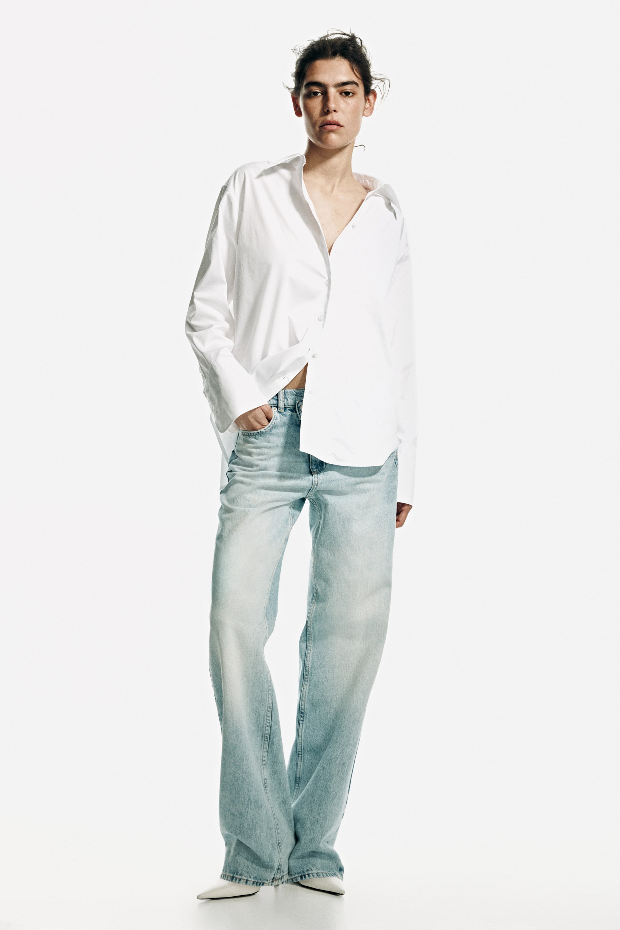View larger image: "A white oversized button-down shirt with a pointed collar, long sleeves, and wide cuffs is worn partially unbuttoned and tucked into light wash, high-waisted, wide-leg jeans. The jeans cascade over white pointed-toe shoes."