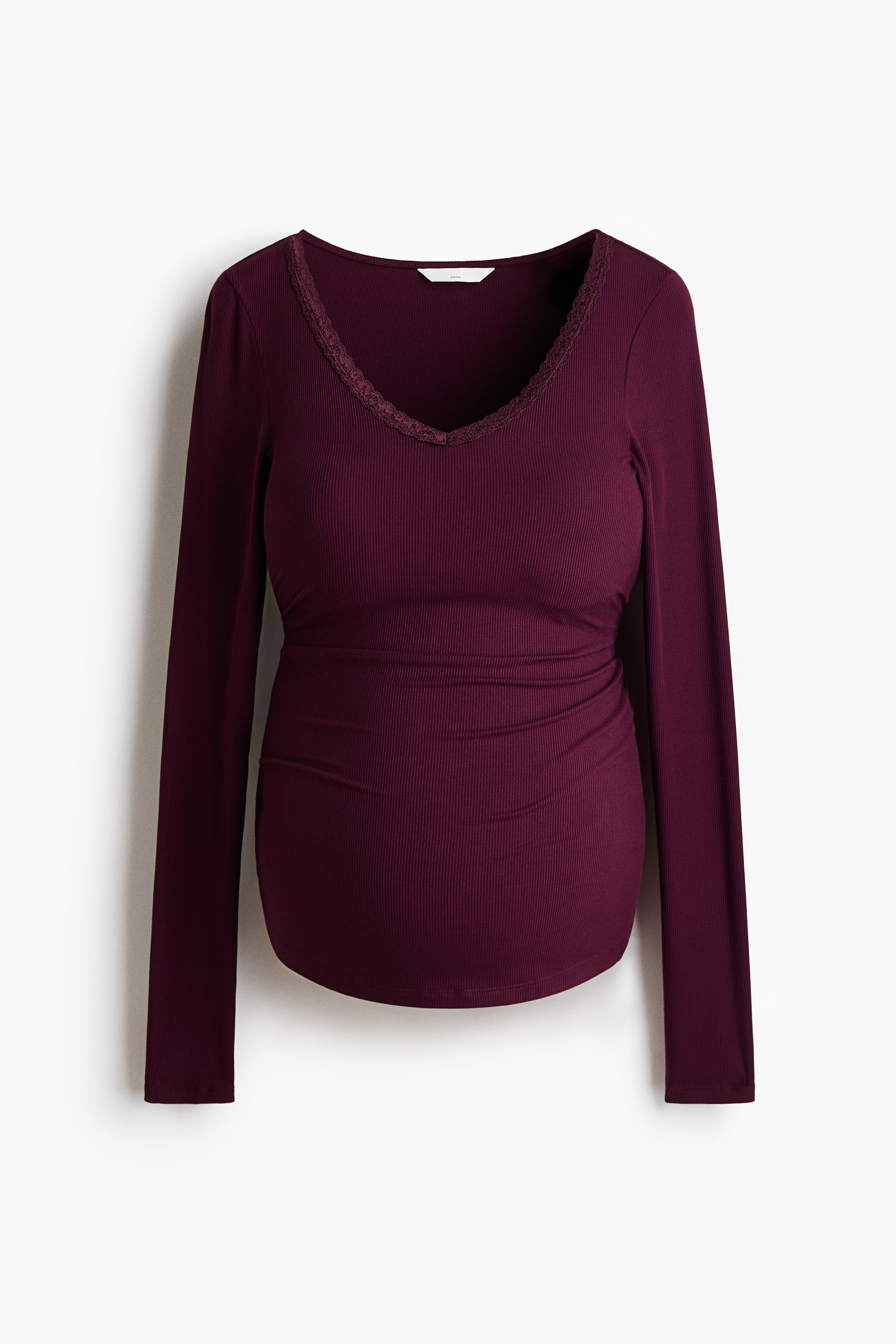 A burgundy, fitted, long-sleeve top in ribbed jersey is being worn by the model, stretching over her pregnant belly. The top features a V-neckline with delicate lace trim and is paired with light-wash, wide-leg jeans.