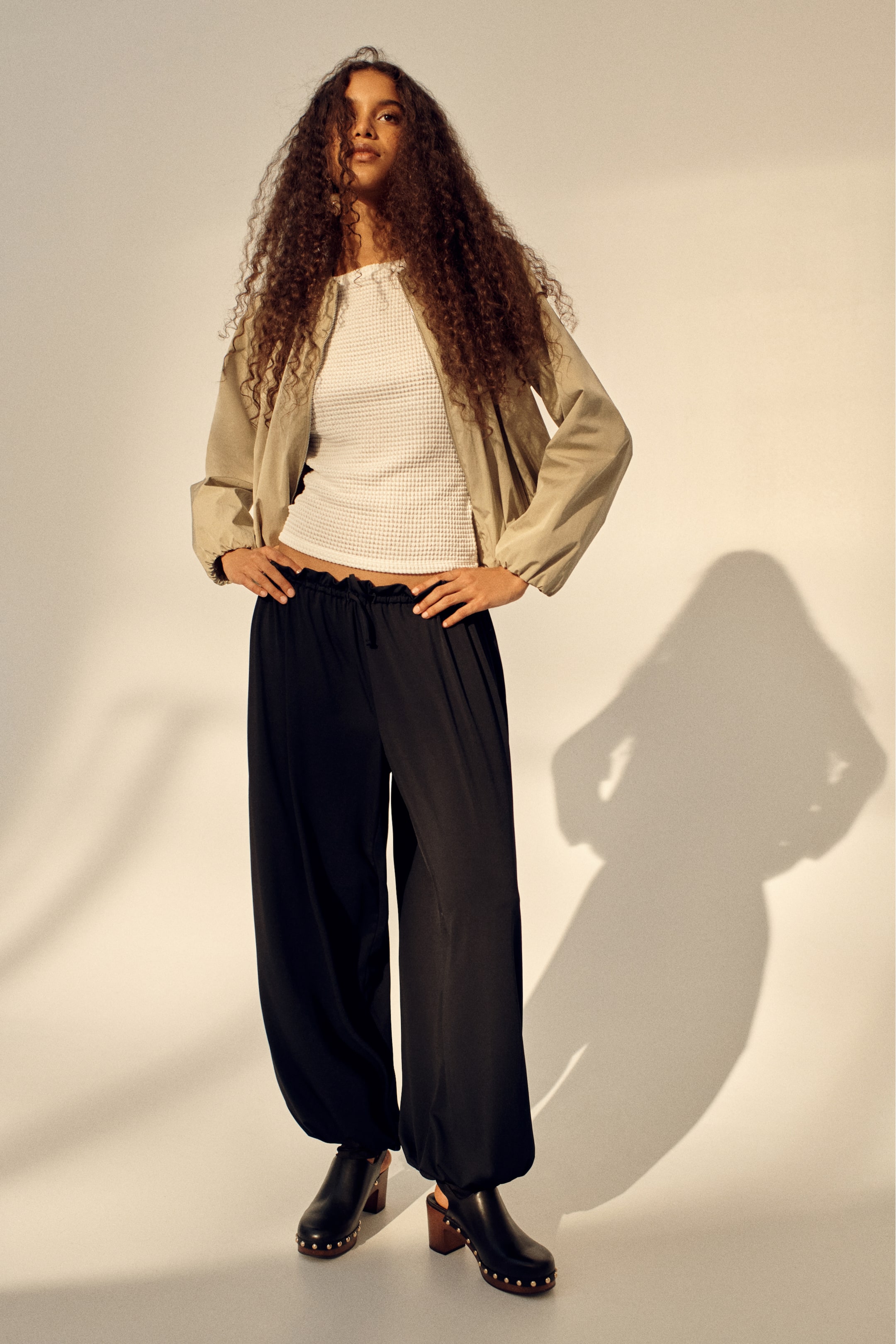 הצגת תמונה גדולה יותר: חולצת סריג וופל לבנה עם צווארון עגול מעט מתנפח ושוליים קצרים, מתאימה בצורה צמודה ונוחה מתחת למעיל בצבע חום בהיר.