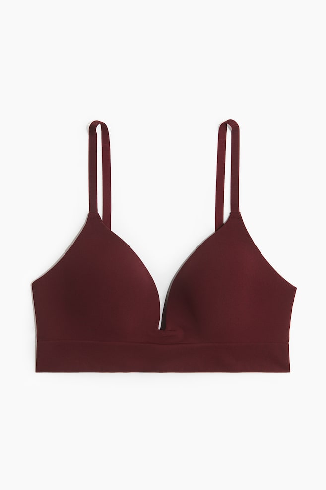 A burgundy bralette is presented from the front, featuring smooth, seamless cups with a deep V-neckline, thin adjustable shoulder straps, and a wide underband. - 1